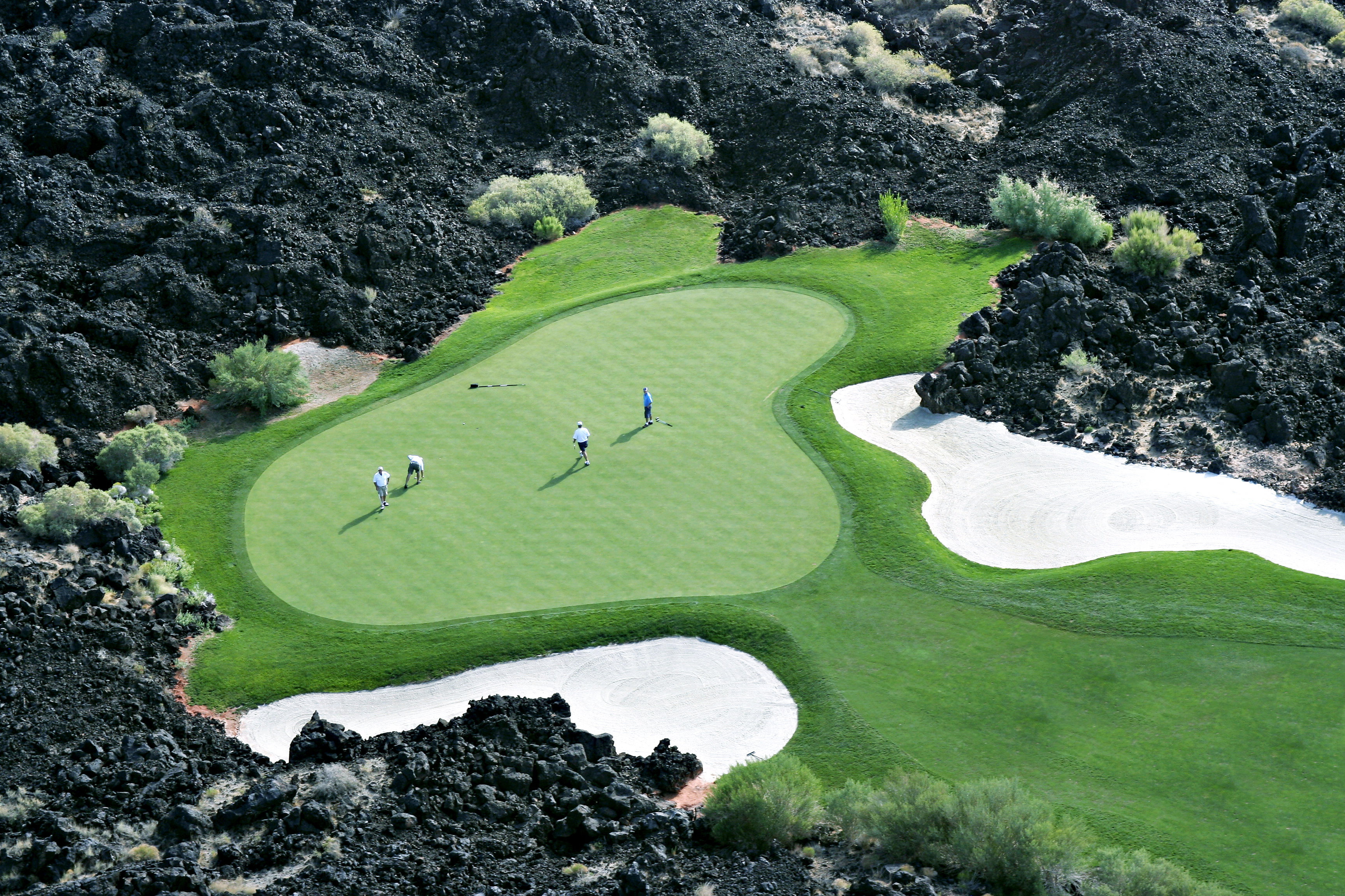 Manicured golf green surrounded by natural dark rock formations and sparse desert foliage