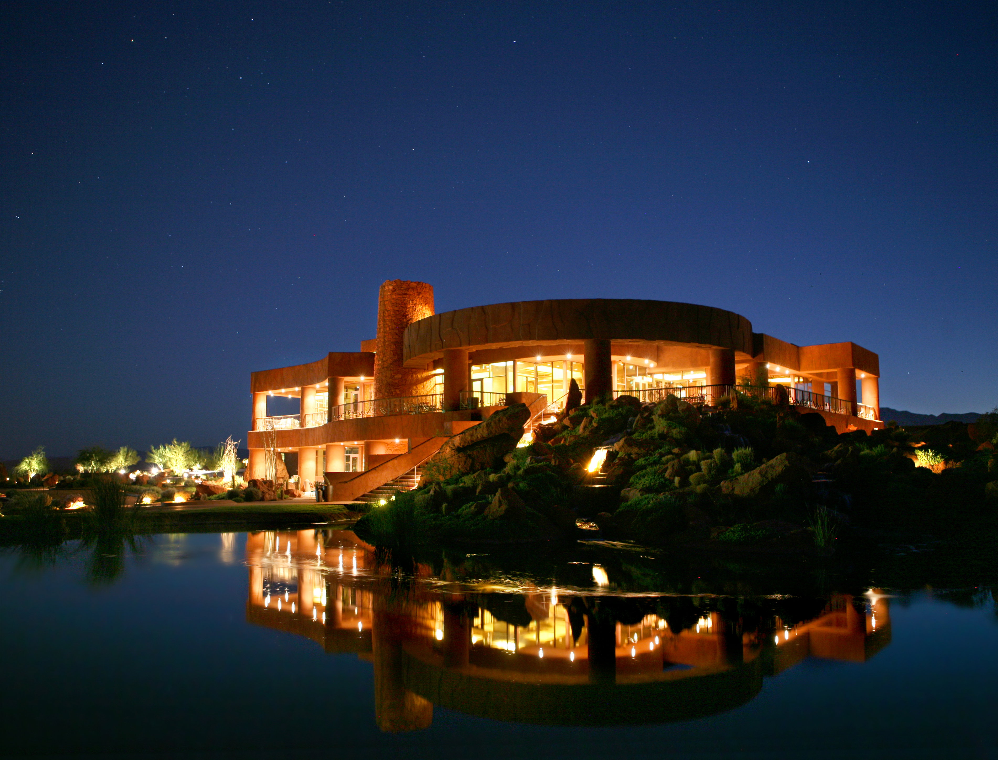 Architectural residence featuring a curved facade, extensive glass panels, and exterior illumination