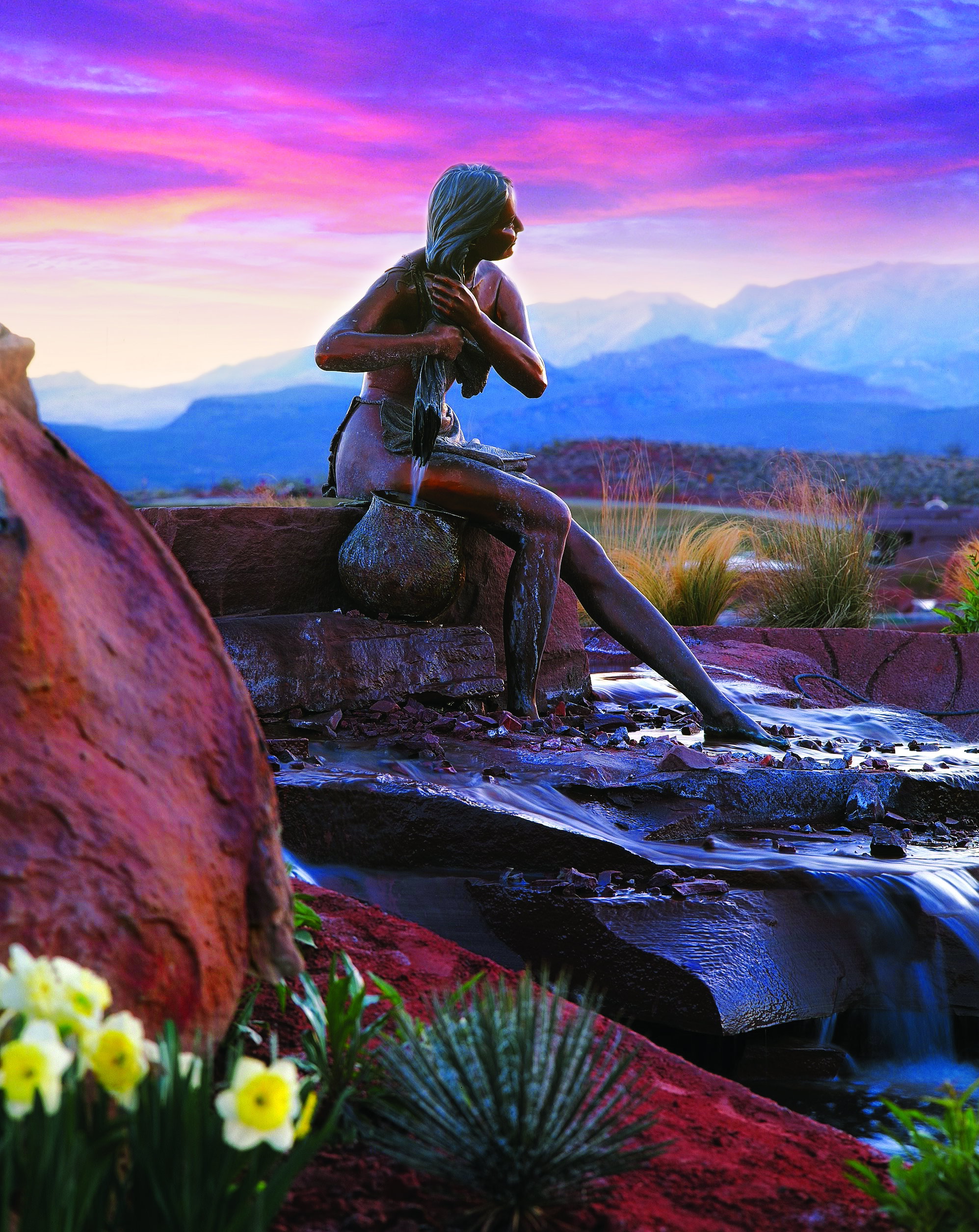 Sculpted bronze figure at water feature with rock landscaping