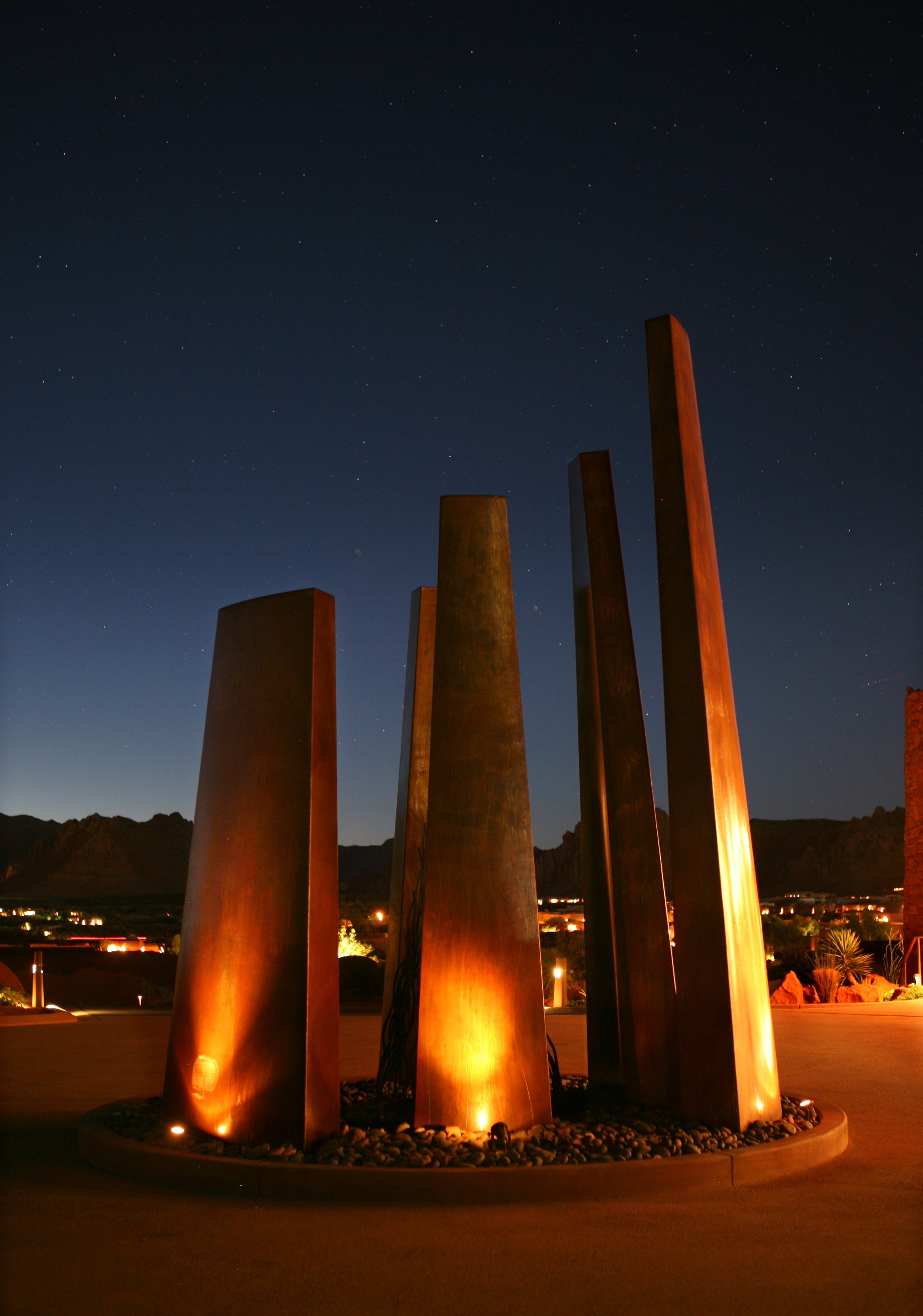 Curved architectural feature with embedded lighting, surrounded by dark river rocks, against a dark sky