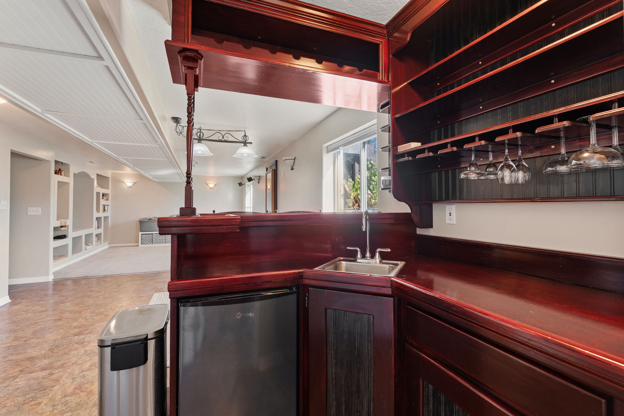 Built-in wet bar featuring rich wood-finish cabinetry, stainless steel sink, and integrated overhead glass racks