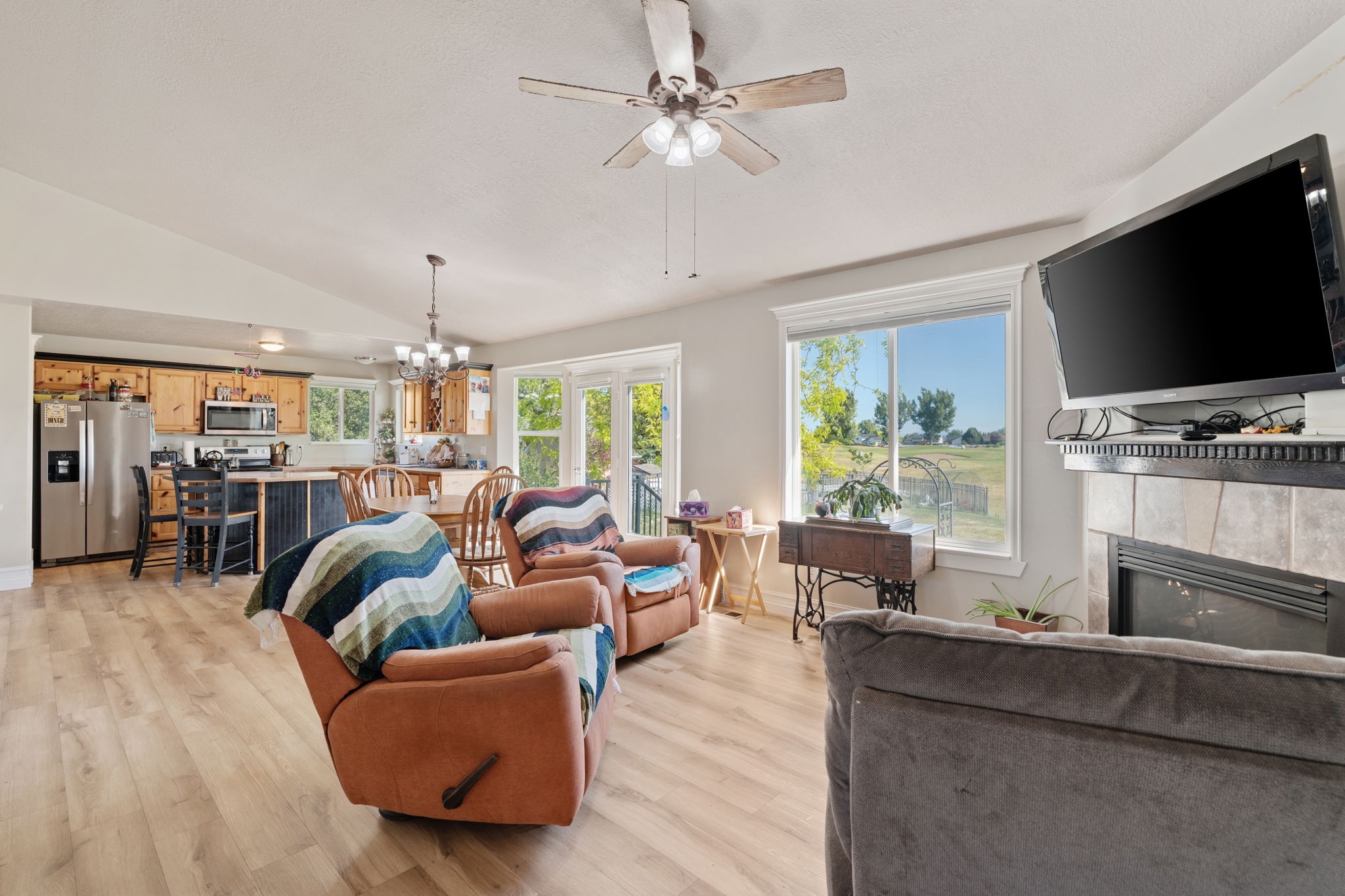 Open-concept living space featuring wood-finish flooring, a ceiling fan with light fixture, and large windows