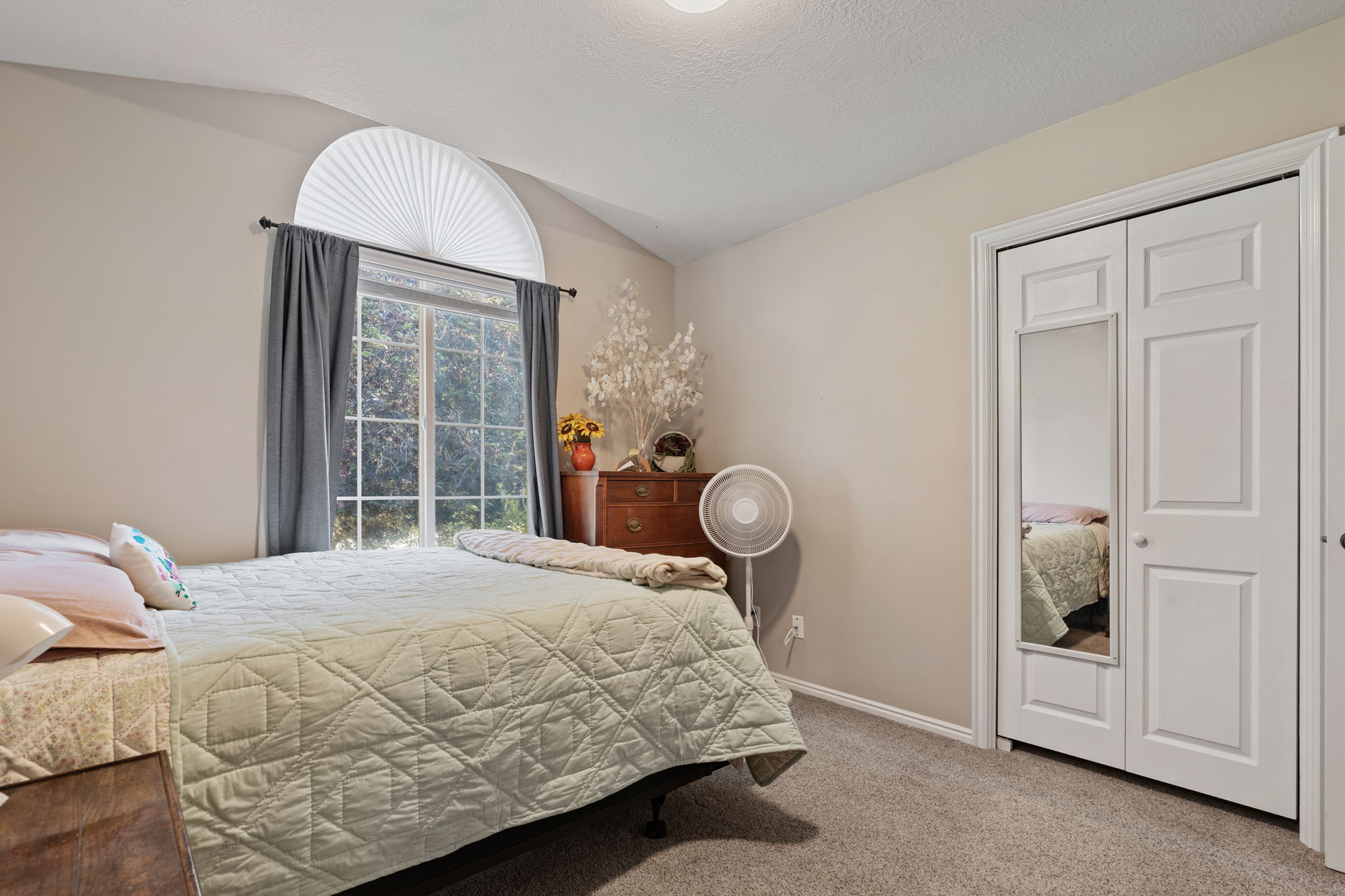 Vaulted ceiling bedroom with a large window featuring an arched transom and pleated shade
