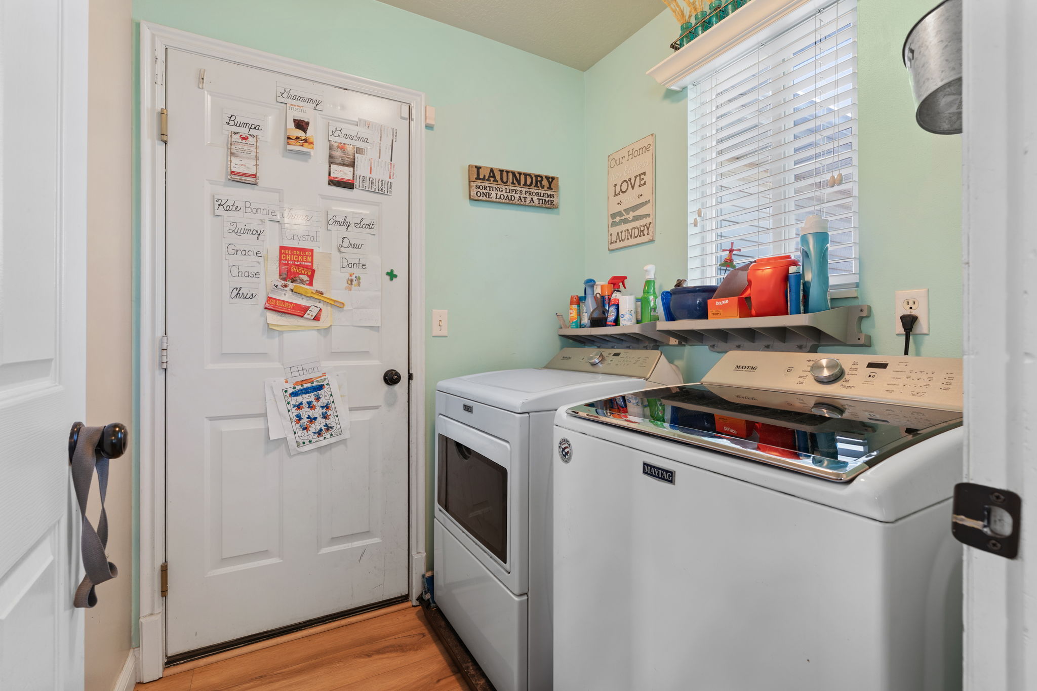 Dedicated laundry area featuring wood-finish flooring, a white window with blinds, and light green walls