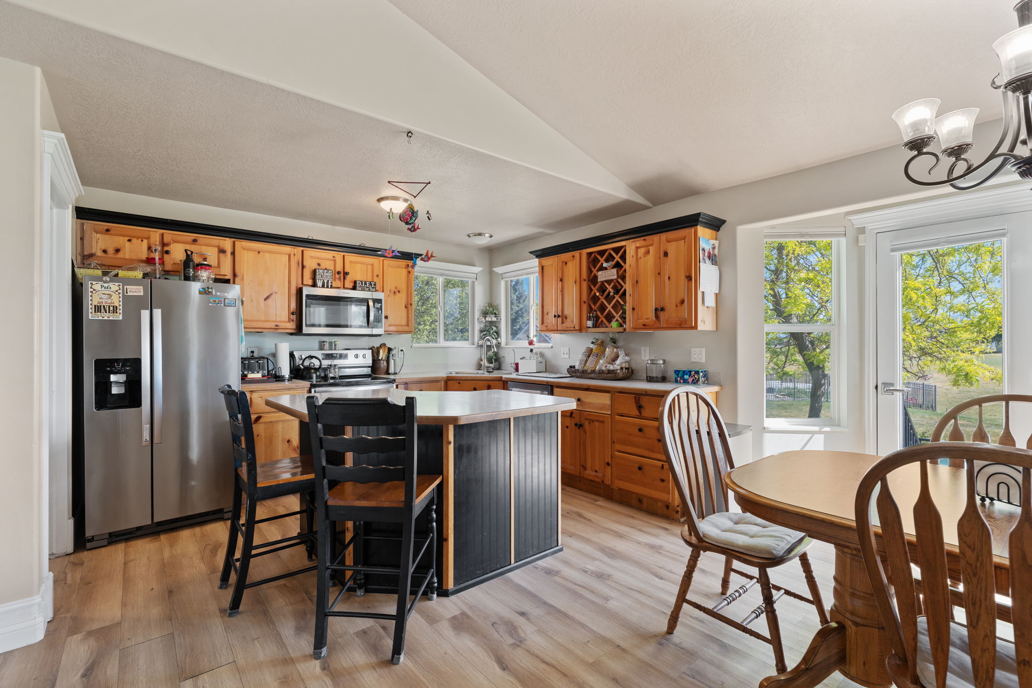 Kitchen featuring wood-finish flooring, natural wood cabinetry with black trim, stainless steel appliances, and a central island with counter seating