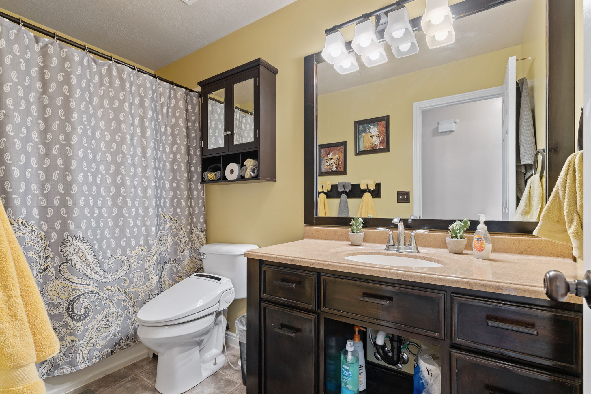 Bathroom featuring a dark wood-finish vanity with an integrated sink, a light-colored countertop, and a large wall-mounted mirror