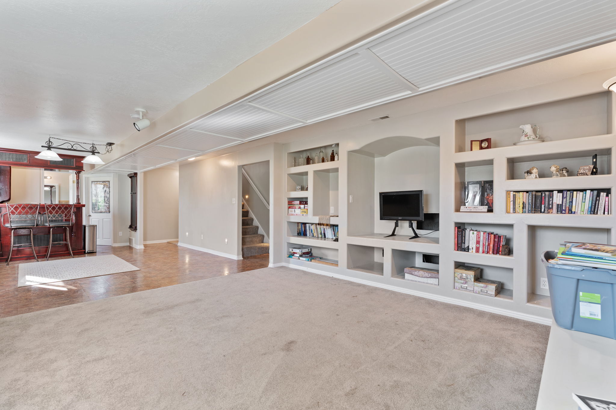 Open-concept space featuring built-in shelving, integrated media niche, carpeted flooring, and a recessed bar area with pendant lighting
