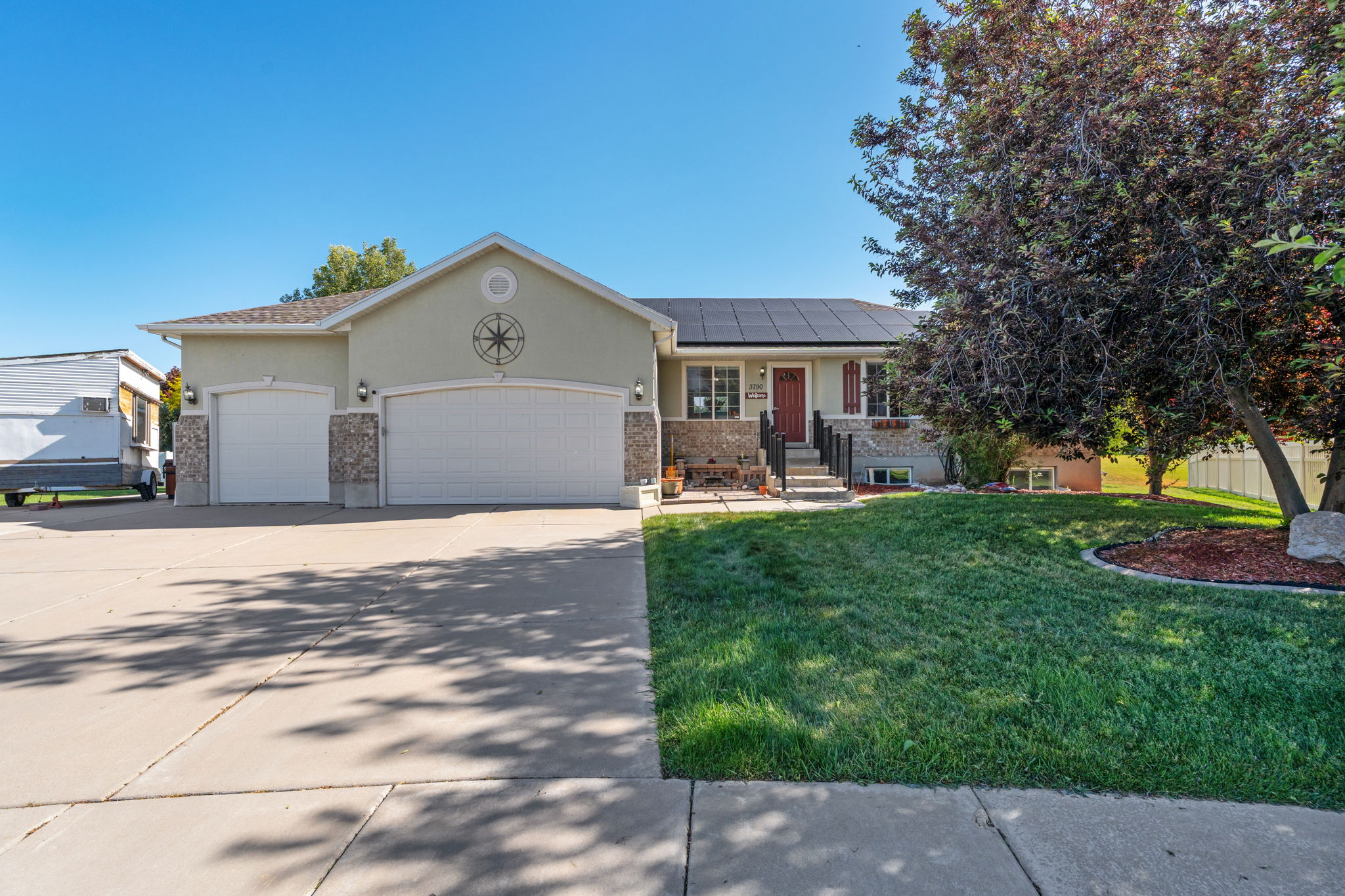 Exterior showcasing a three-car garage, stone accents, and a front entry with a red door