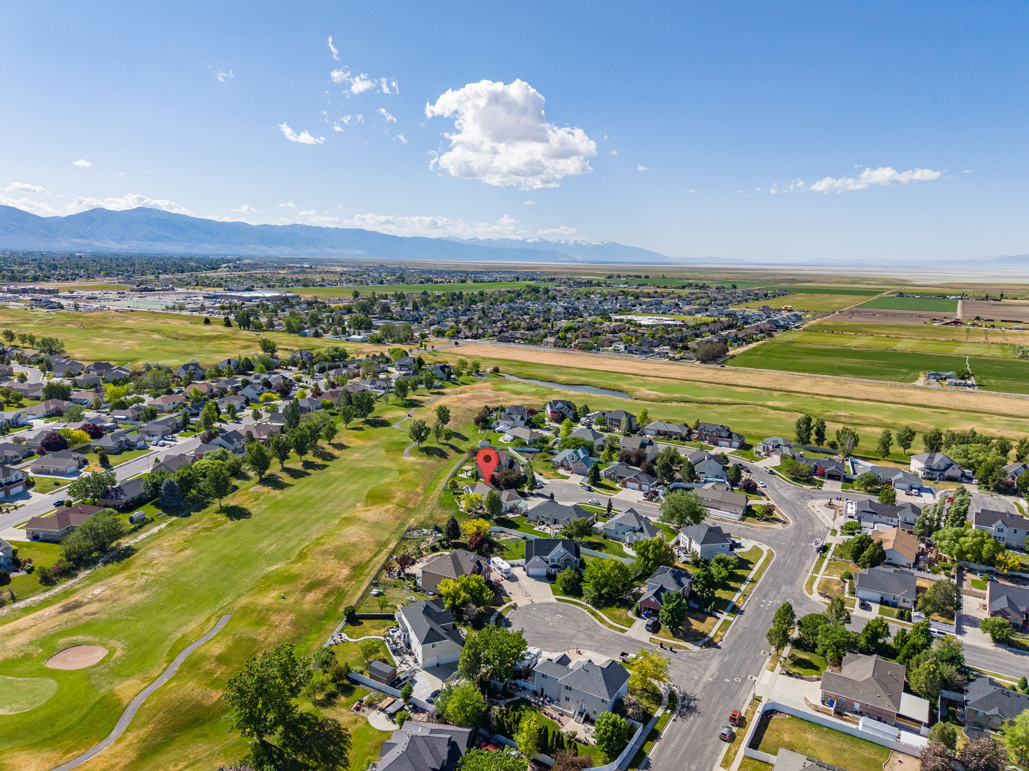 Aerial perspective showcasing a residential neighborhood with a golf course bordering properties, agricultural fields, and distant mountains