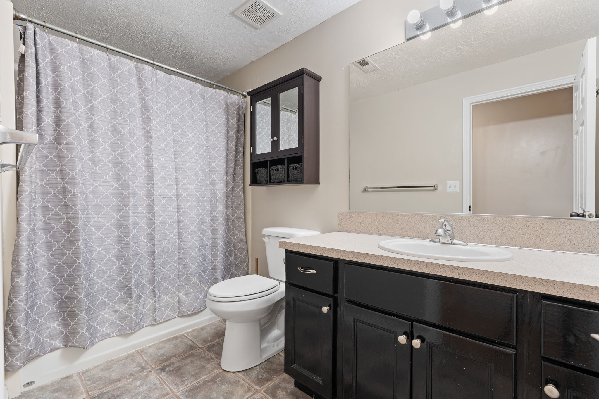 Bathroom featuring a dark wood-finish vanity with an integrated sink, a large wall-mounted mirror, a built-in shower/tub combination, and tiled flooring