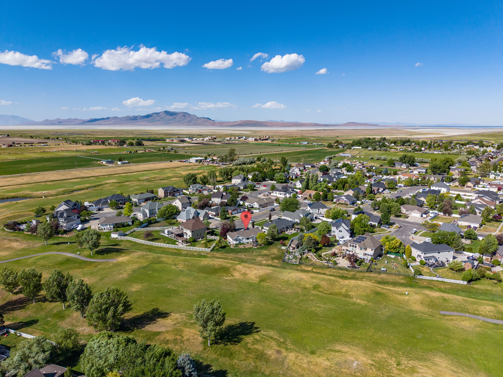 Aerial view showcasing a residential community surrounded by expansive green spaces and distant mountains