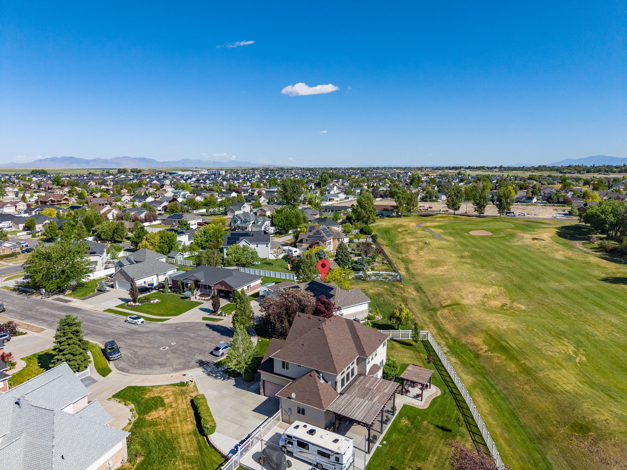 Aerial view showcasing a residential property with a multi-level home, an expansive green space, and distant mountain ranges