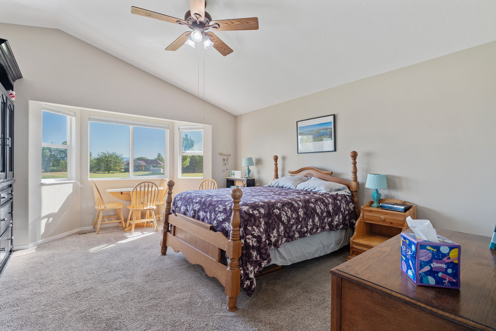 Vaulted ceiling bedroom with a ceiling fan, plush carpet flooring, and a wide window bay