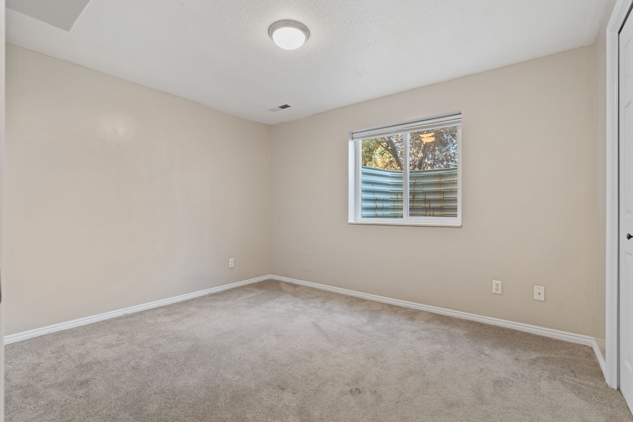 Neutral-toned room featuring light gray carpeting, white baseboards, and a window with a window well