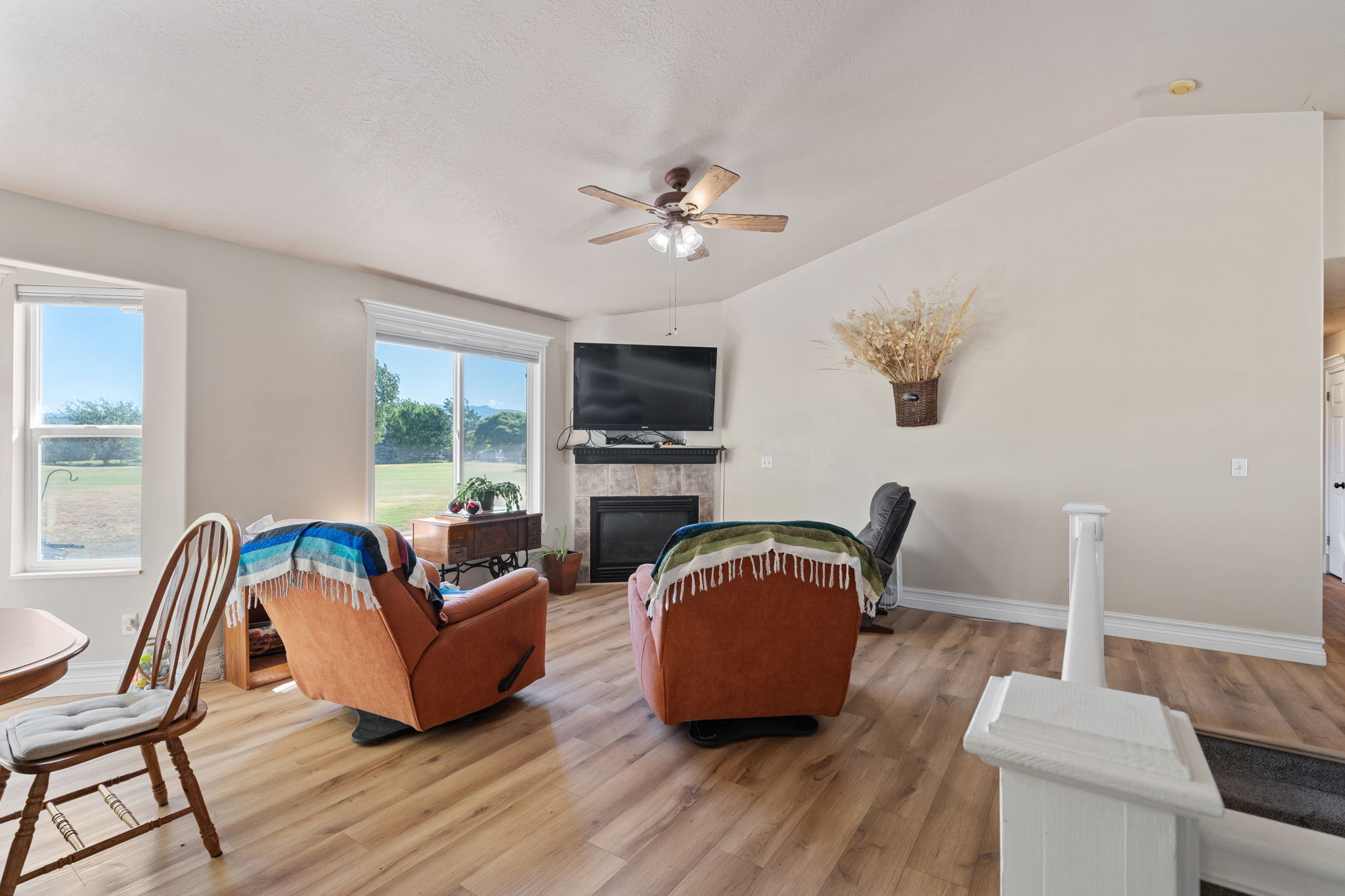 Vaulted ceiling living area featuring wood-finish flooring, a corner fireplace with stone tile surround, and multiple large windows