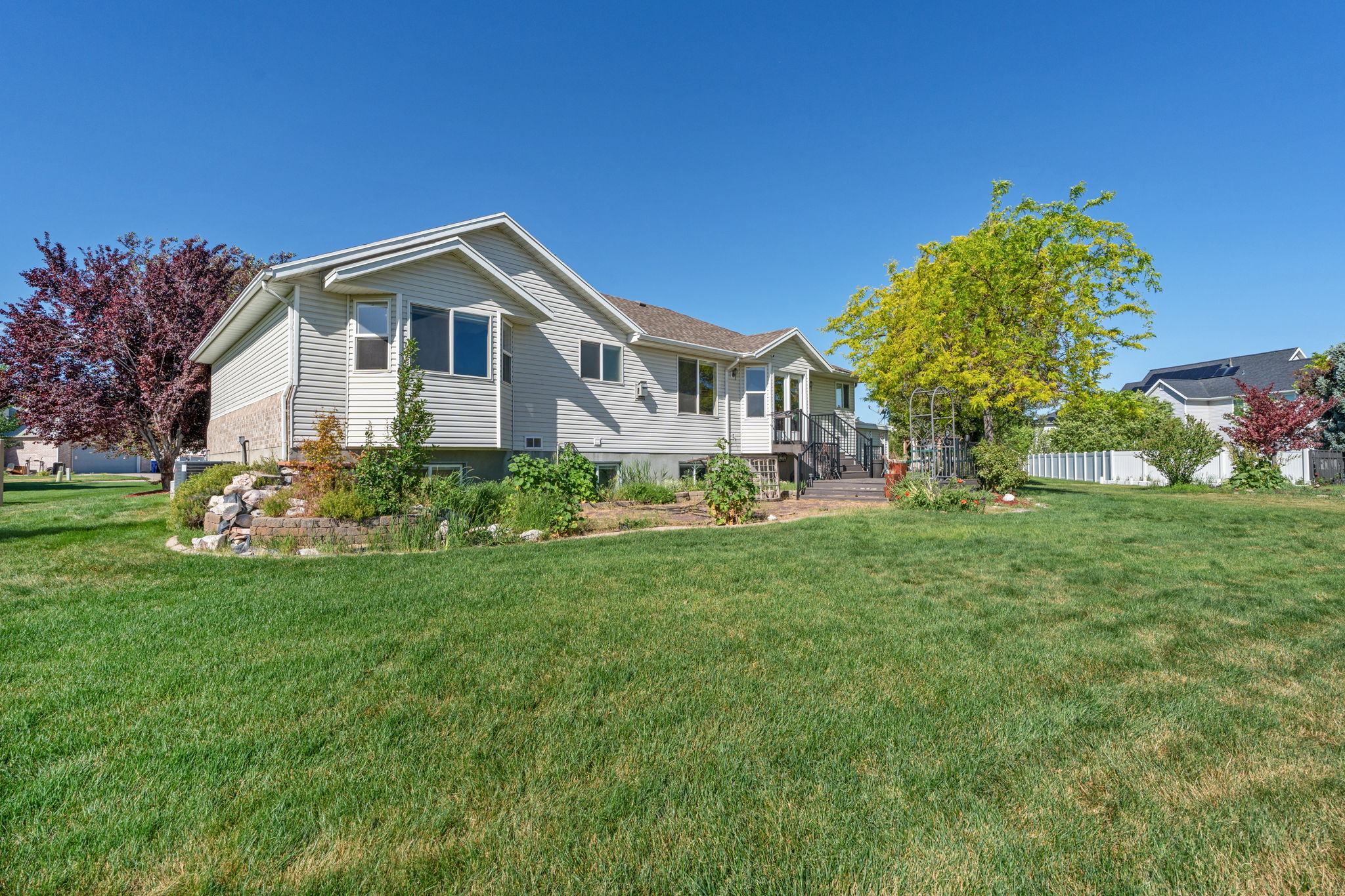 Spacious backyard featuring a manicured lawn, established trees, and a multi-level deck