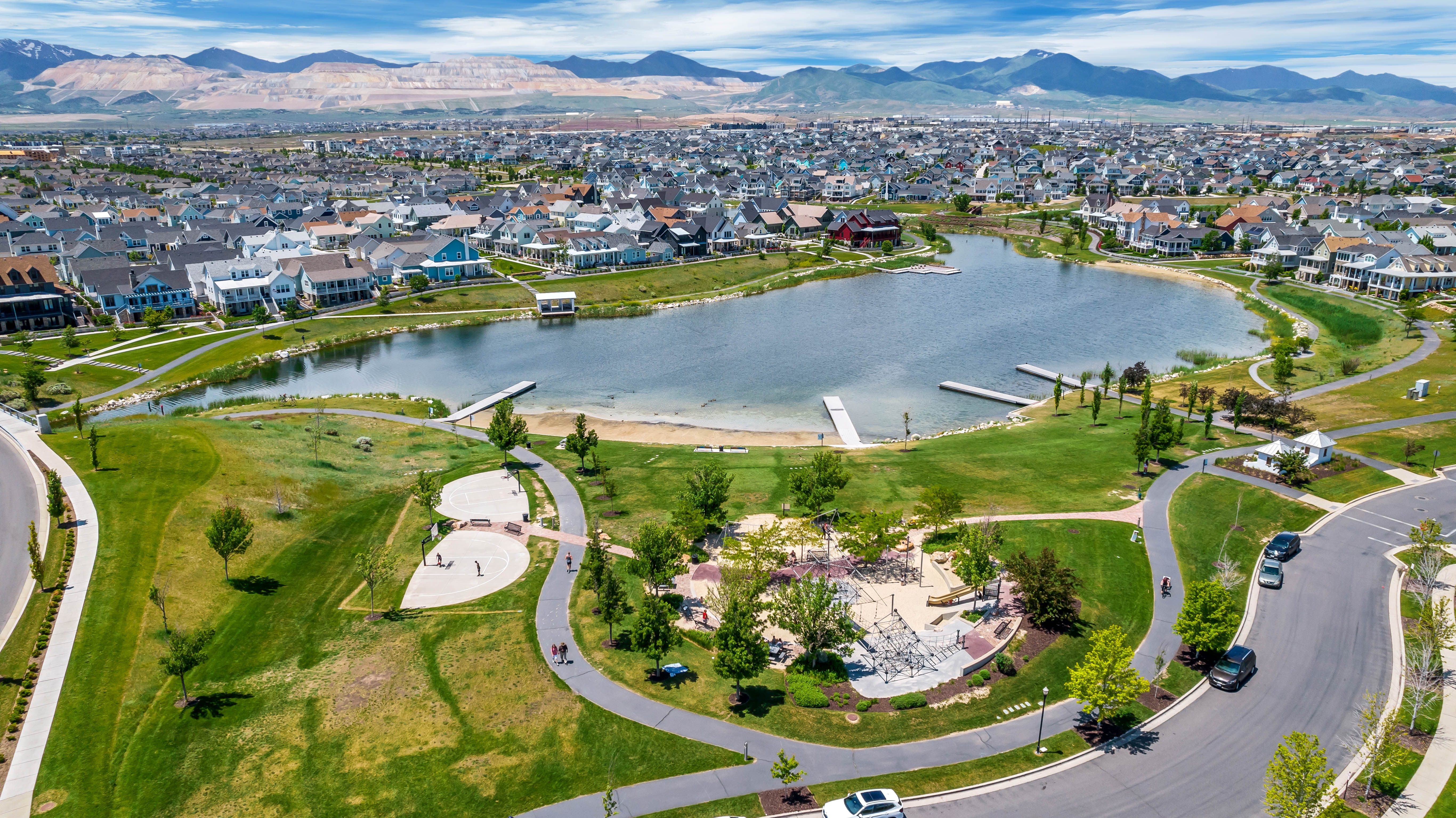 Expansive lakefront community featuring a large water body with multiple docks, surrounding green spaces with walking paths, and distinct residential architecture