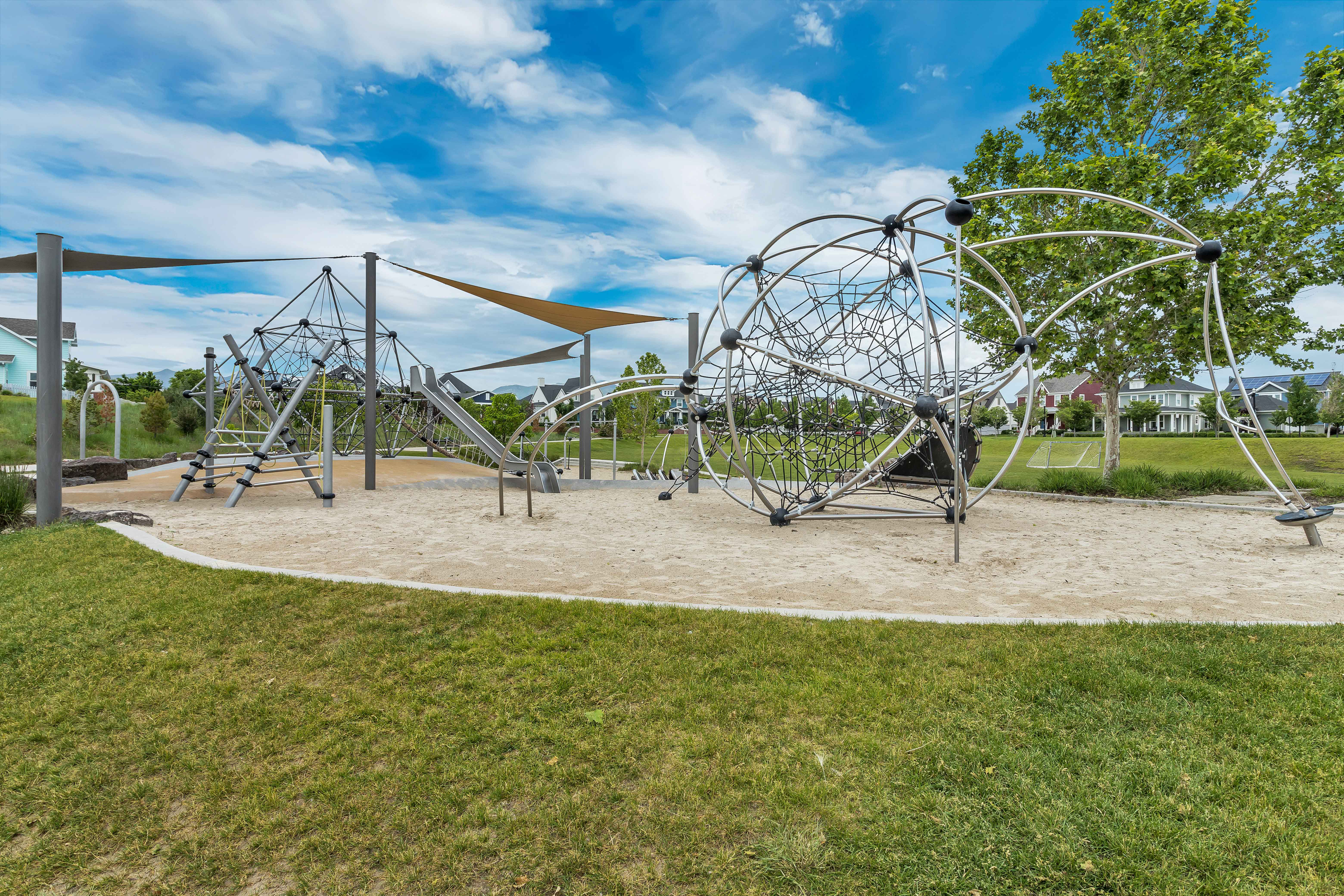 Community playground featuring modern climbing structures, shade sails, and a sand base