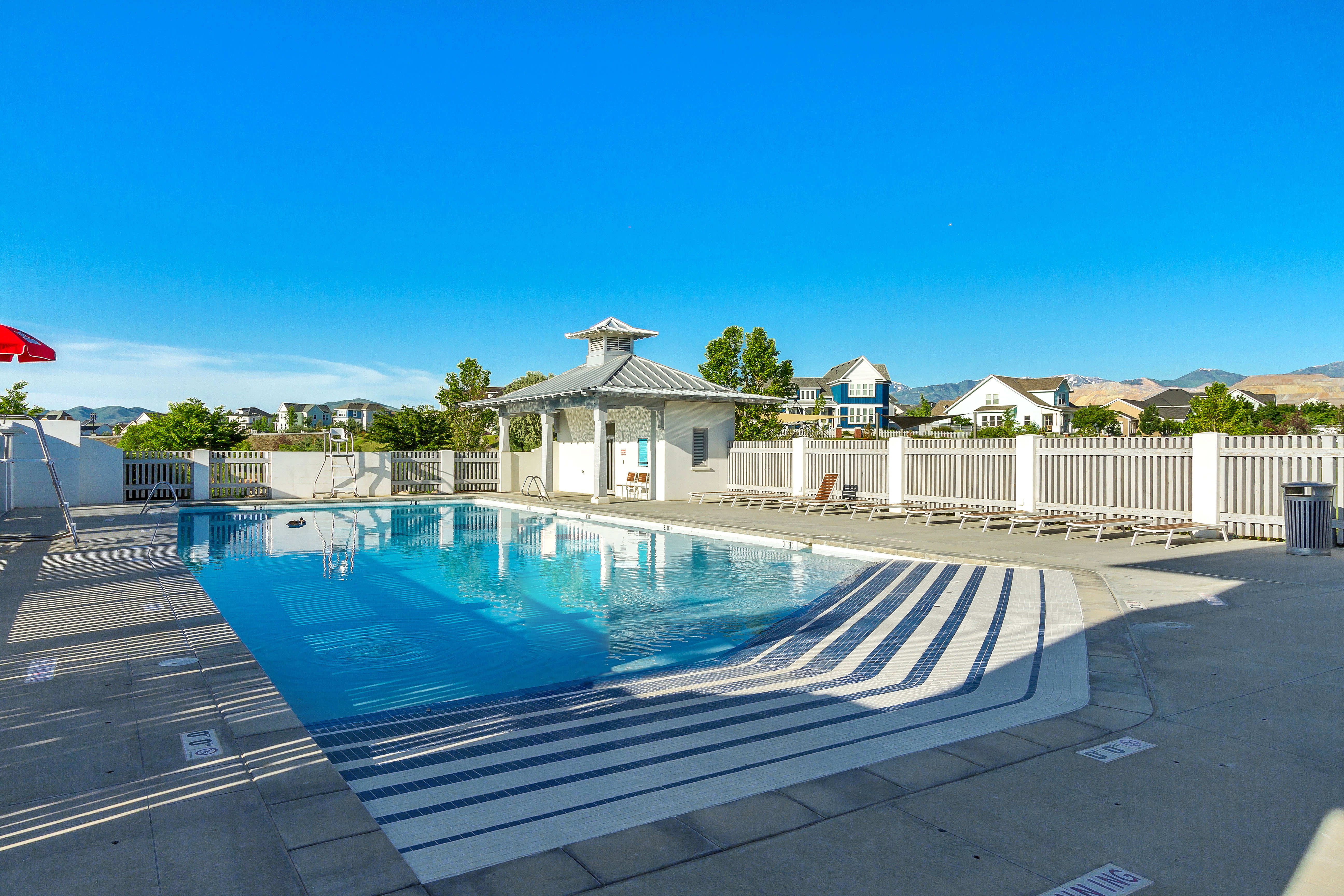 Outdoor swimming pool with patterned steps, surrounded by a white picket fence, a small poolside structure, and concrete decking