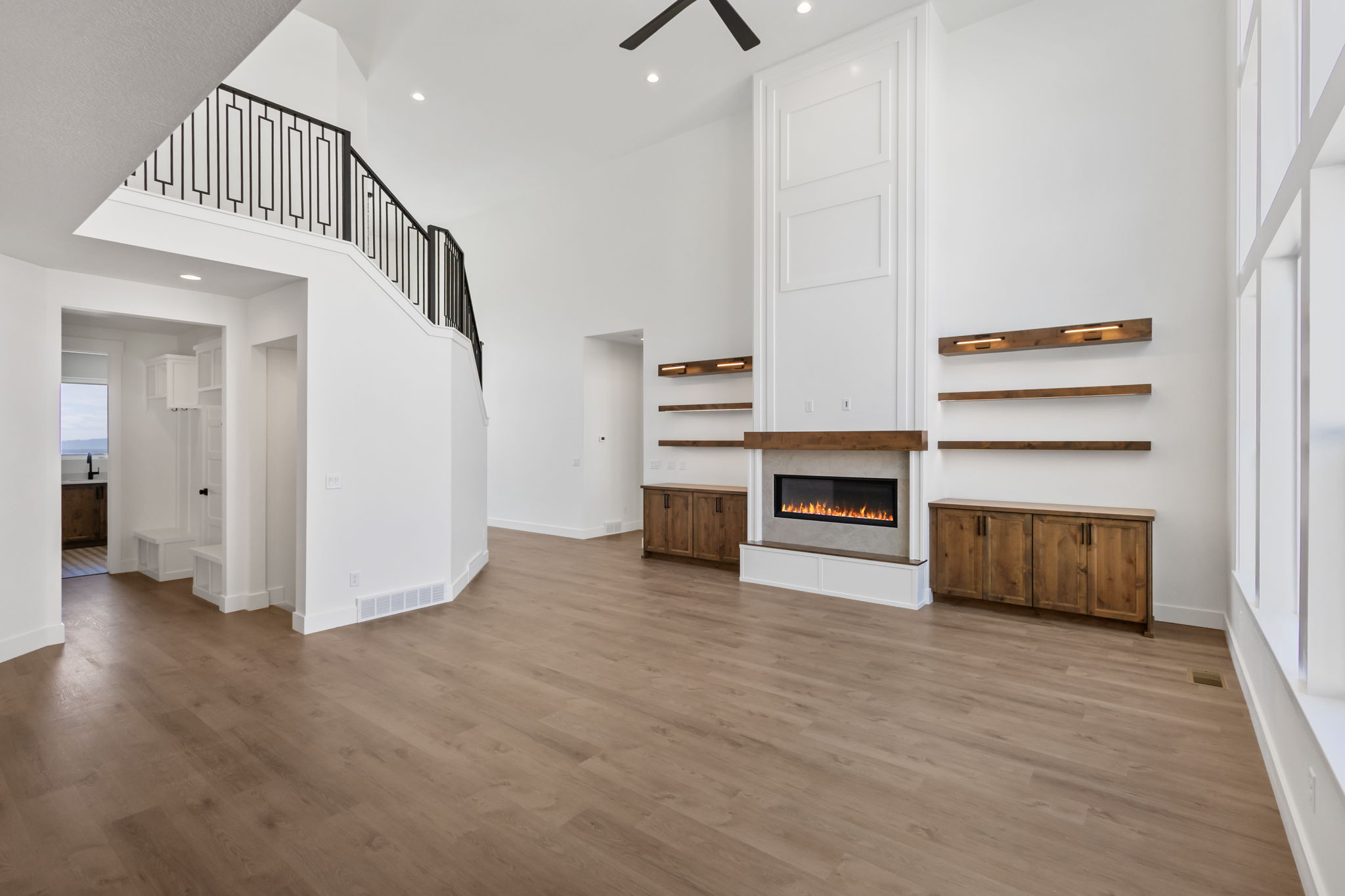 Great room featuring a tall vaulted ceiling, wood-finish flooring, a contemporary fireplace with a wood mantle, custom built-in cabinetry, and a striking staircase with decorative metal railing