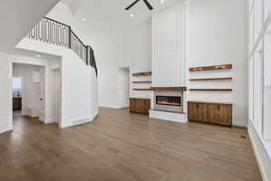 Great room featuring a tall vaulted ceiling, wood-finish flooring, a contemporary fireplace with a wood mantle, custom built-in cabinetry, and a striking staircase with decorative metal railing