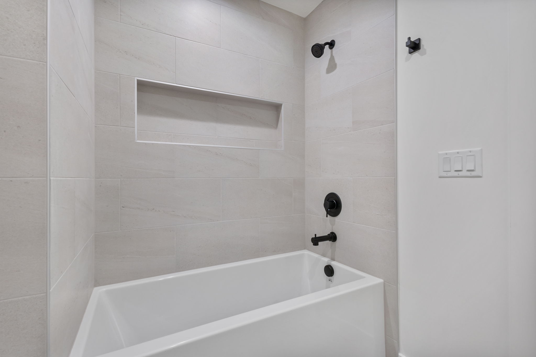 Bathtub with matte black fixtures, light-toned wall tiling, and an integrated shower niche