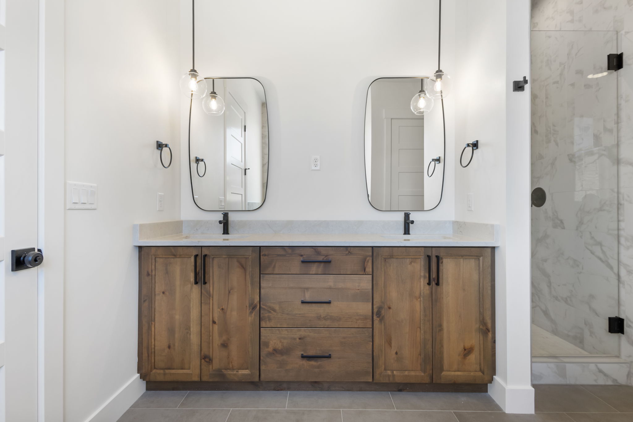 Dual wood-finish vanities with light stone countertops, integrated sinks, and matte black hardware