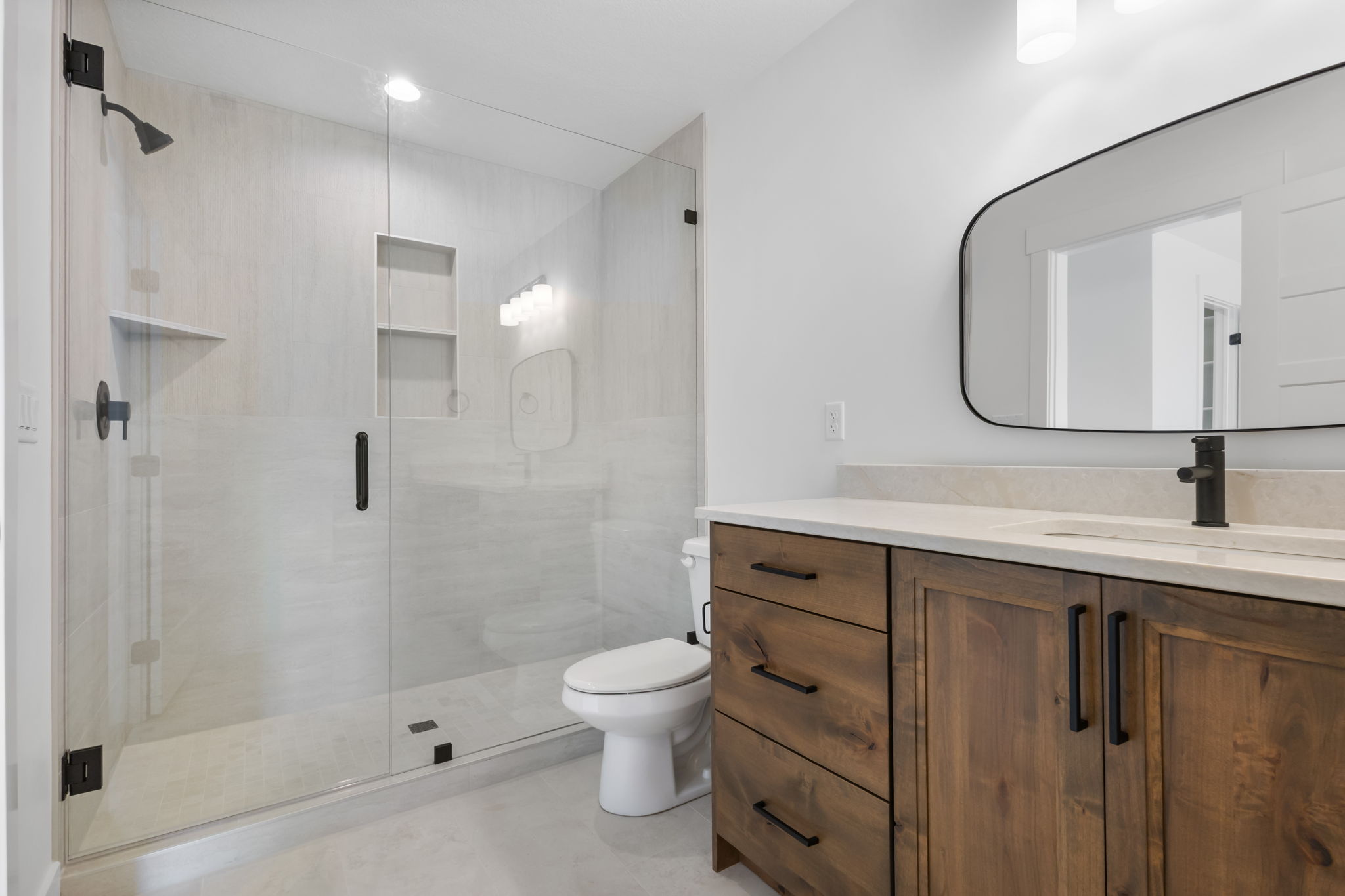 Modern bathroom featuring a frameless glass shower enclosure with matte black fixtures, a built-in shower niche, and a corner shelf