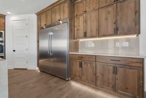 Spacious kitchen featuring floor-to-ceiling wood cabinetry, a stainless steel side-by-side refrigerator, white countertops, and wood-finish flooring