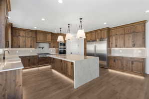 Gourmet kitchen featuring a large central island with pendant lighting, wood-finish cabinetry, stainless steel appliances, and wood-finish flooring