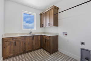 Laundry area featuring wood cabinetry, light-toned countertops, a matte black faucet, and patterned floor tiles