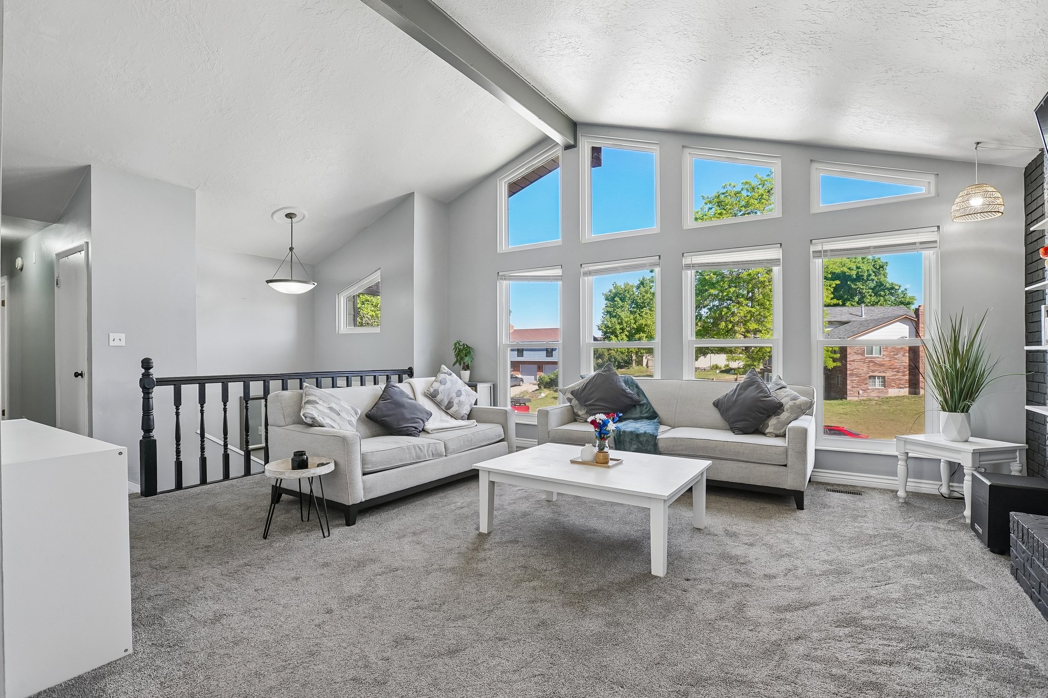 Vaulted ceiling living room featuring expansive window arrays, carpeted flooring, and a black painted baluster railing