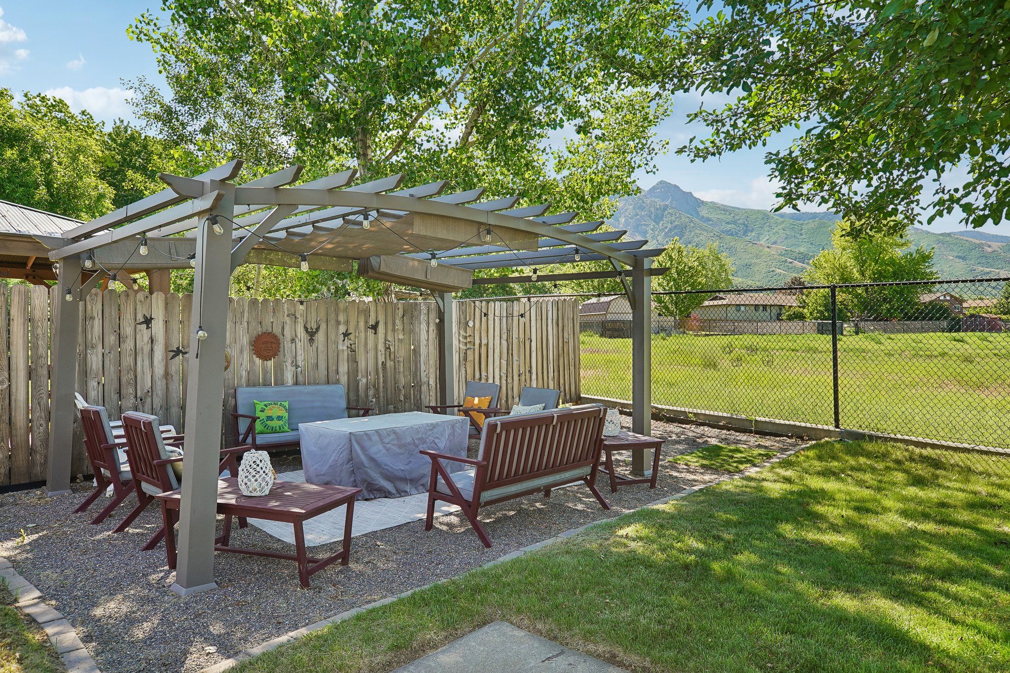 Outdoor living space featuring a gray pergola with string lighting, a gravel patio, and a privacy fence