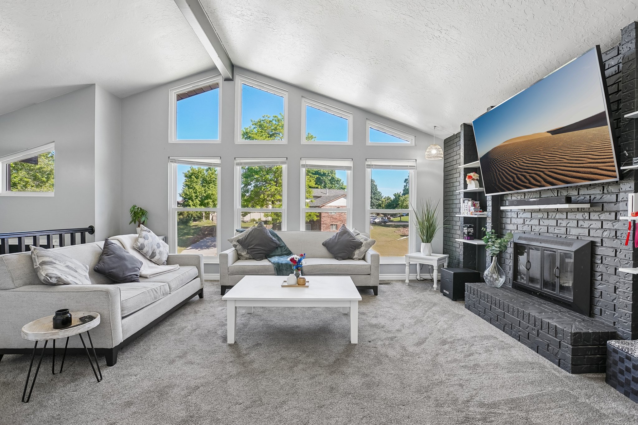 Vaulted ceiling living area featuring a black brick fireplace, integrated shelving, and large picture windows
