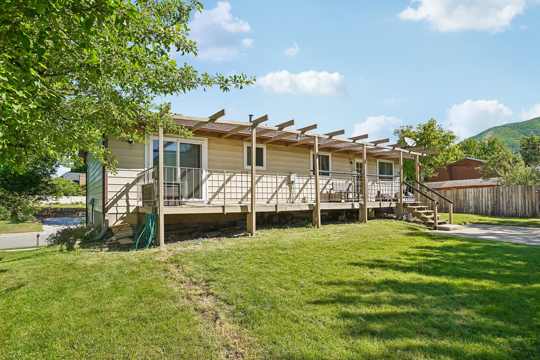 Rear exterior featuring an expansive wood deck with pergola, multiple sliding glass doors, and durable siding