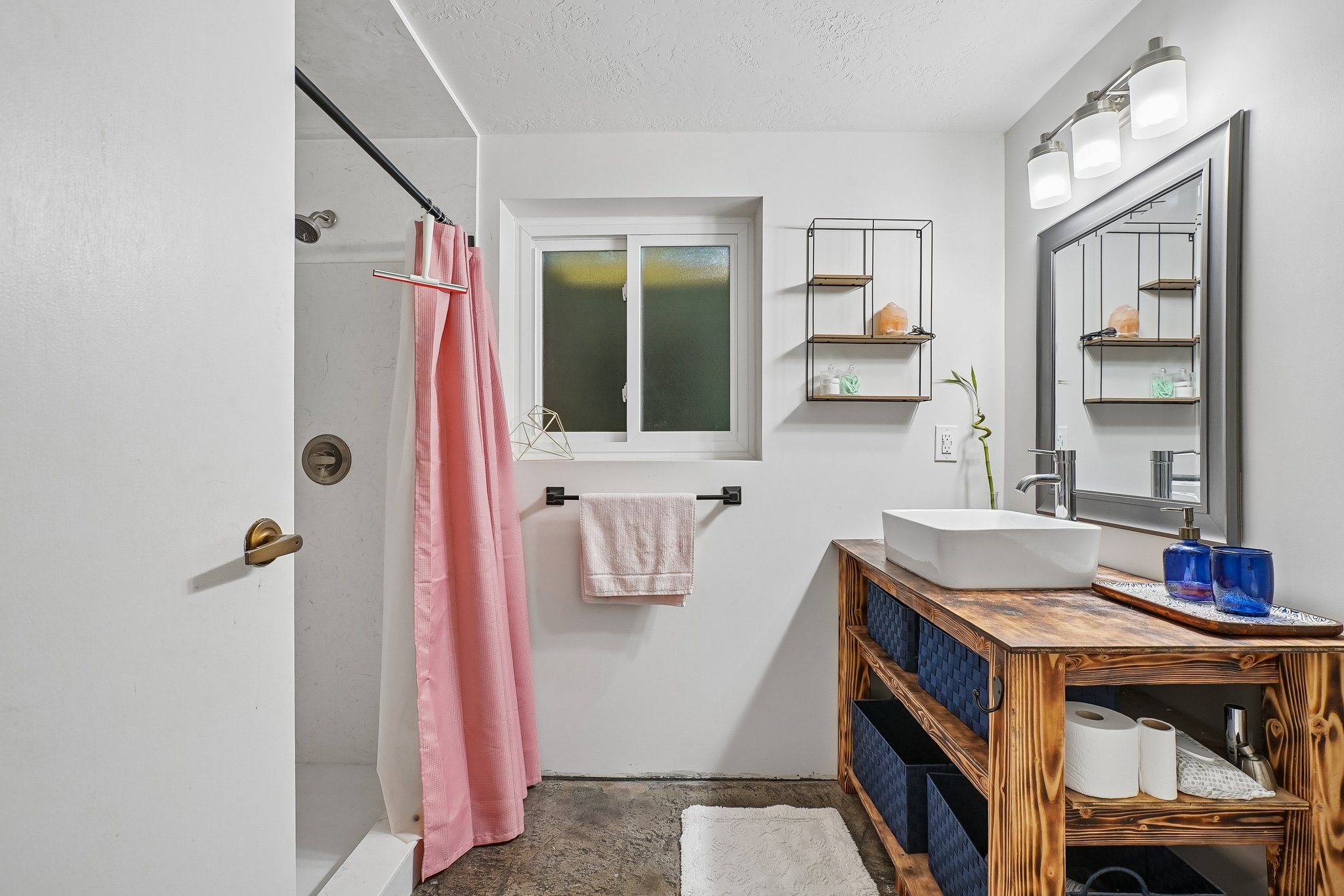 Bathroom featuring a shower with bronze fixtures, a rectangular window with frosted glass, and a vanity with a rectangular vessel sink and wood-finish open shelving