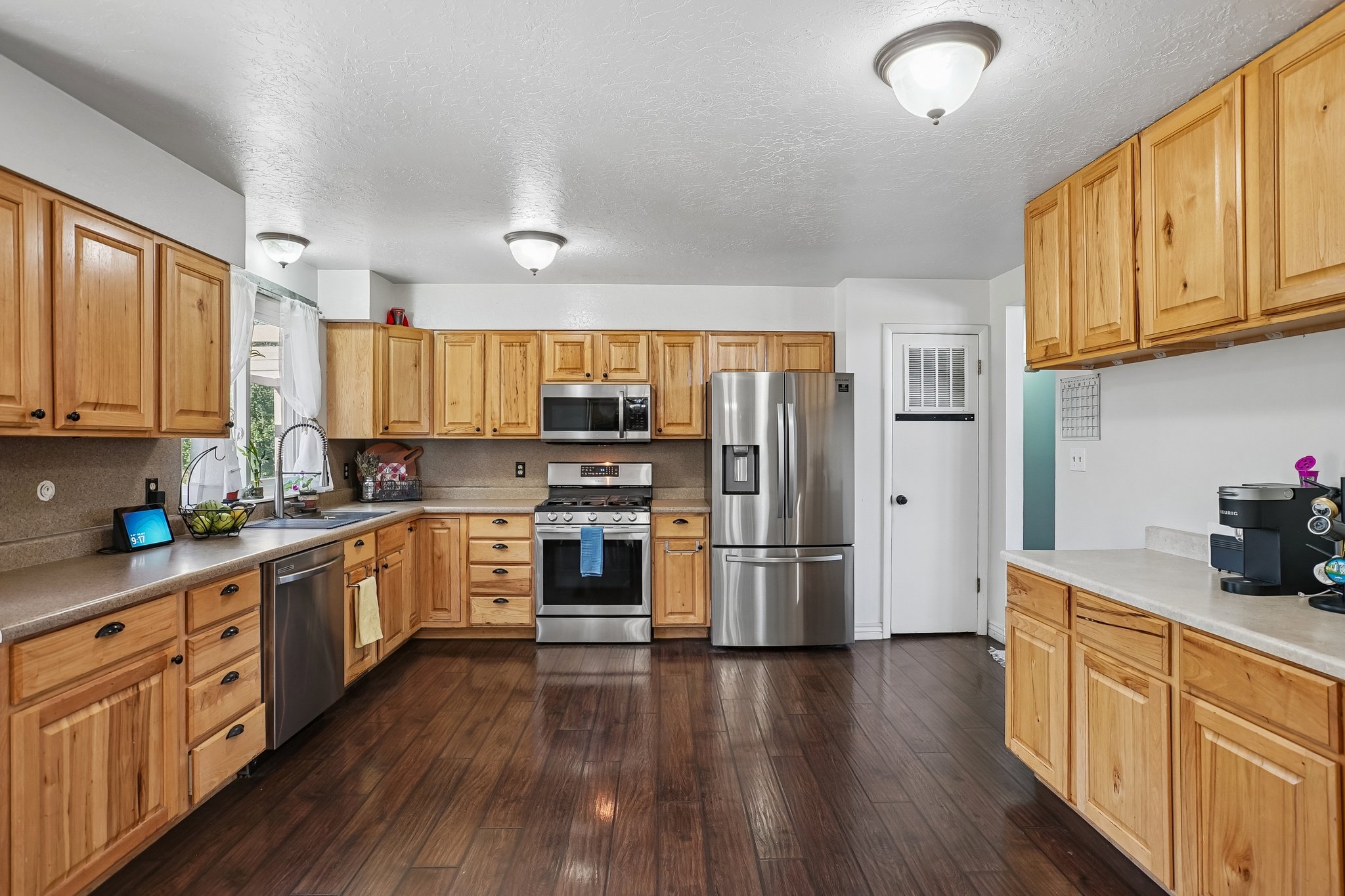 Kitchen featuring wood-finish flooring, light wood cabinetry, stainless steel appliances, neutral countertops, and flush mount lighting