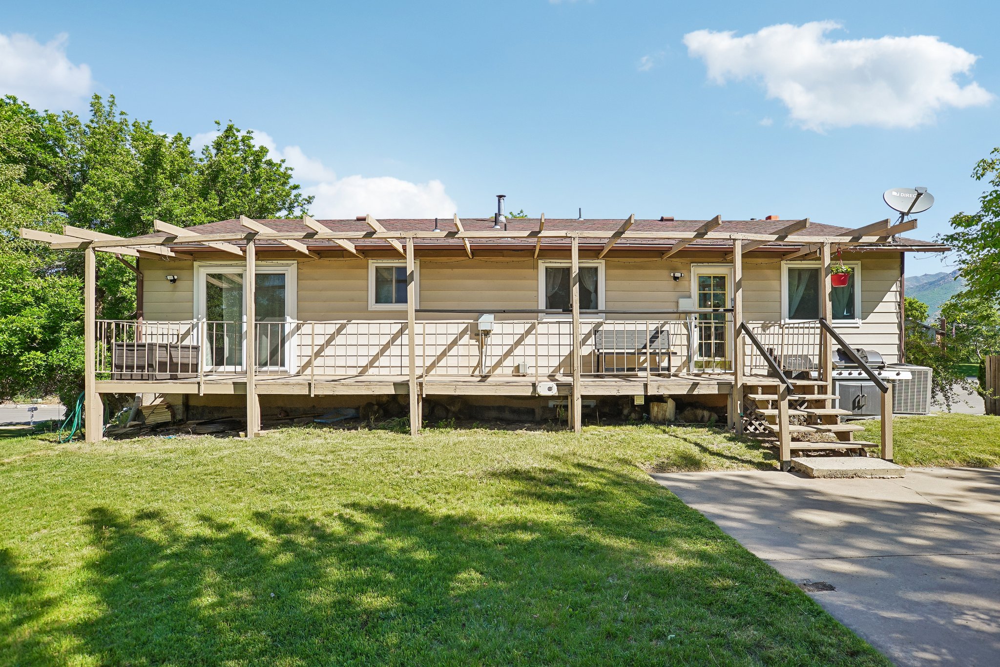 Rear exterior featuring a full-width wood deck with pergola, two sets of sliding glass doors, and exterior stairs to ground level