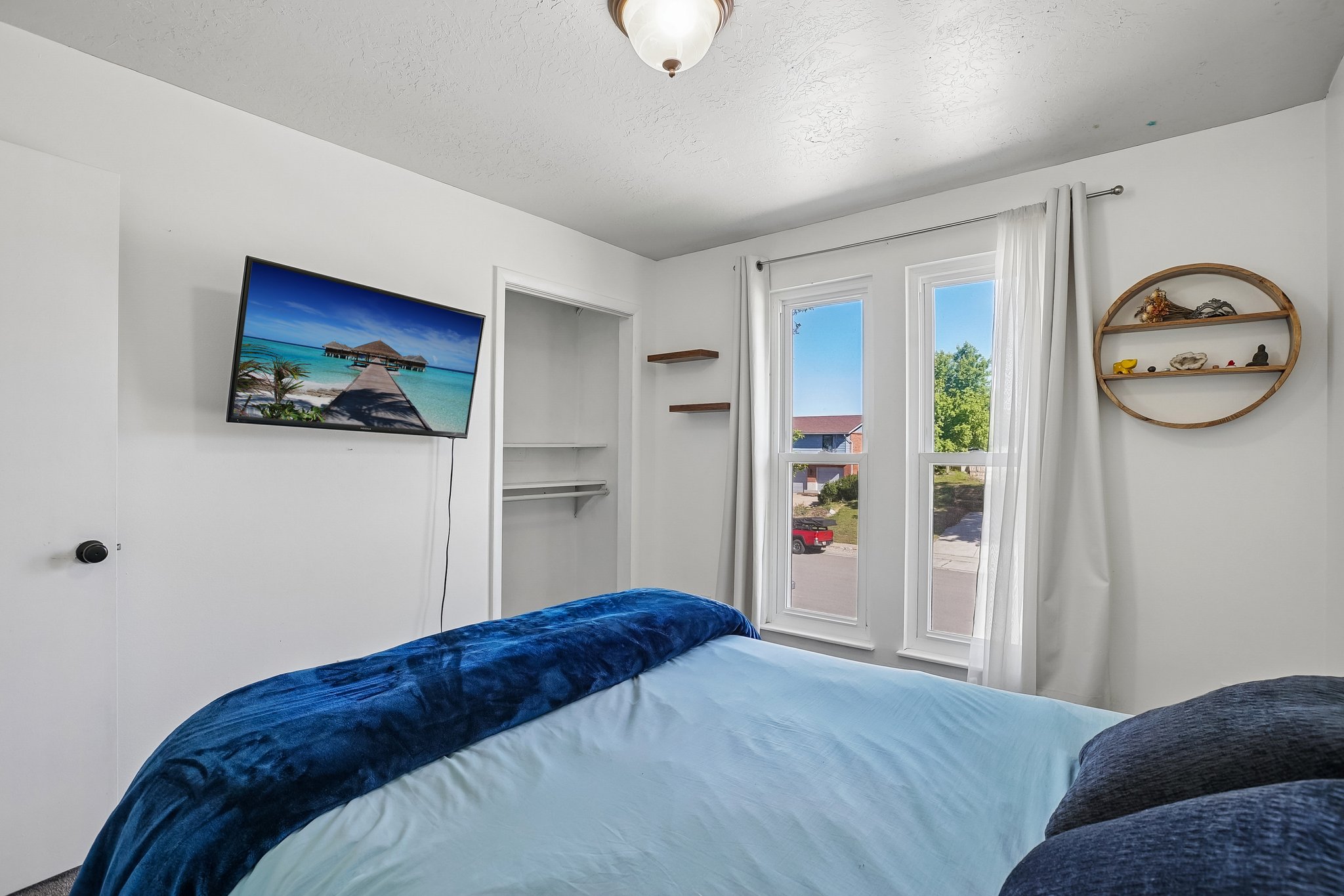 Bright bedroom featuring two large windows, white walls, built-in closet shelving, and a ceiling-mounted light fixture