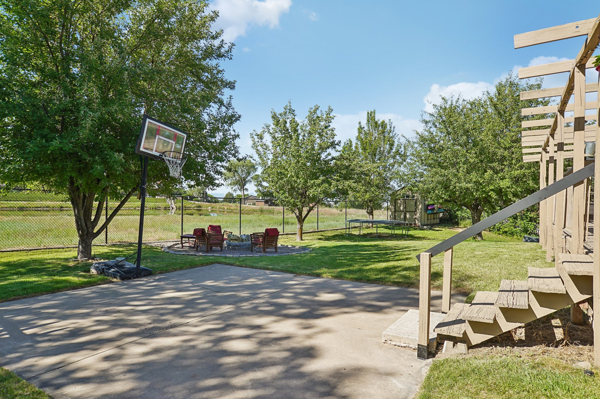 Expansive backyard featuring a concrete patio, a stone fire pit area, and mature trees