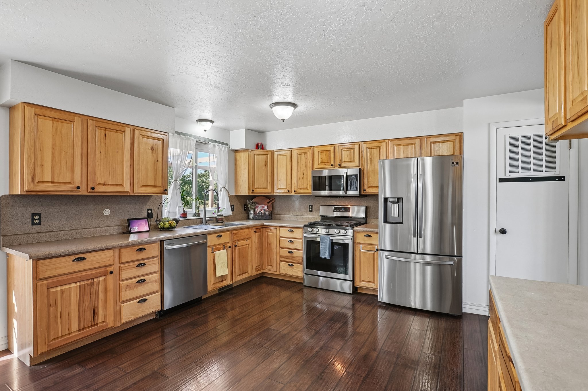 Kitchen featuring wood-finish flooring, light wood cabinetry, stainless steel appliances, a double basin sink, and ample countertop space