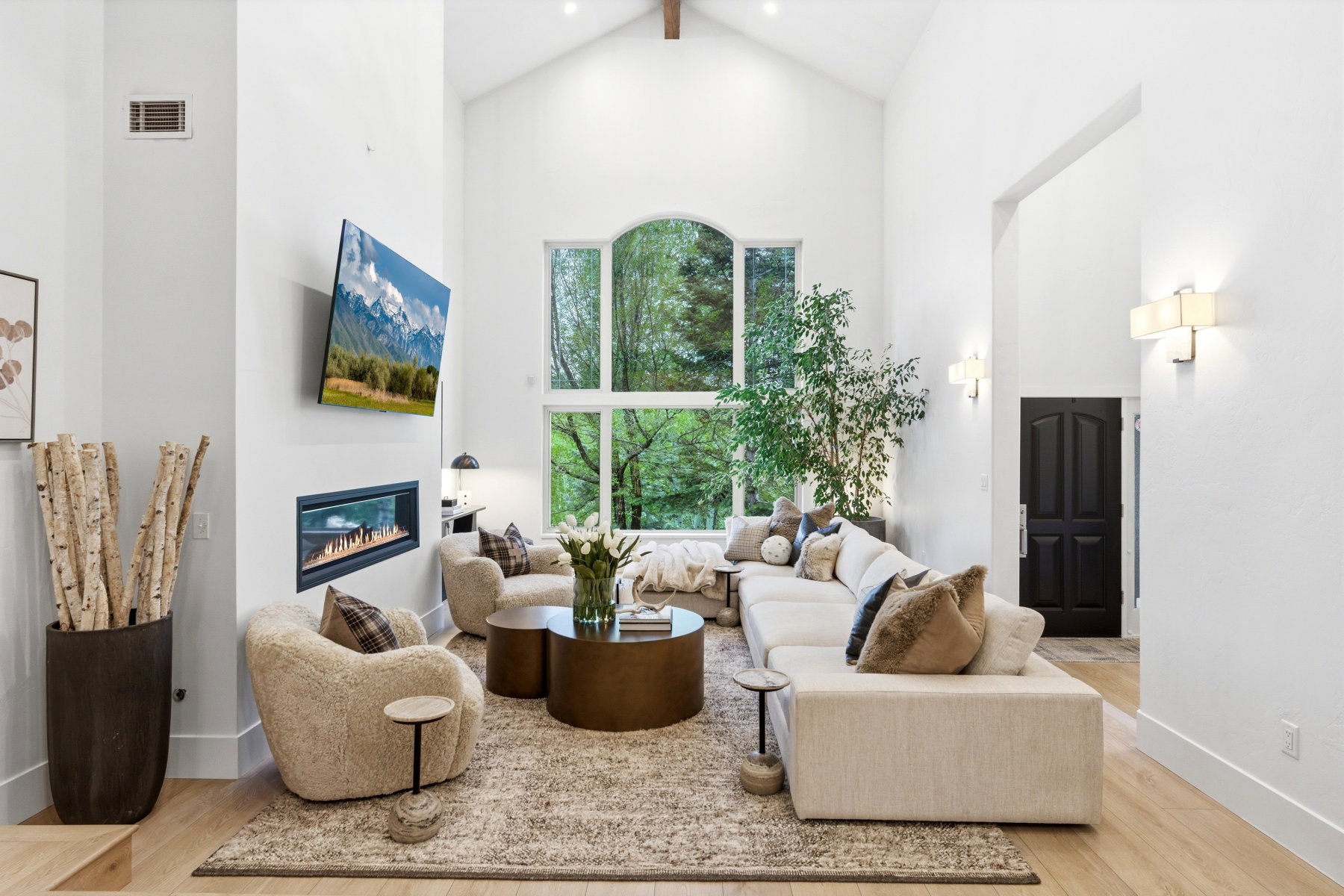 Vaulted ceilings with an exposed beam, a linear fireplace, and expansive windows showcasing surrounding greenery