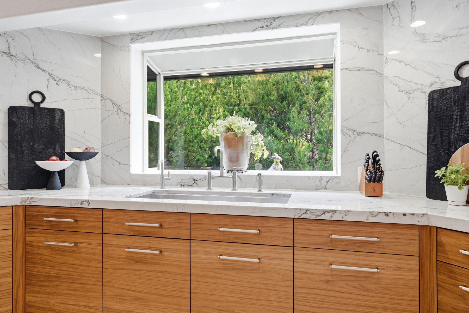 Kitchen featuring custom wood cabinetry with horizontal hardware, stone countertops with integrated sink, and a large picture window