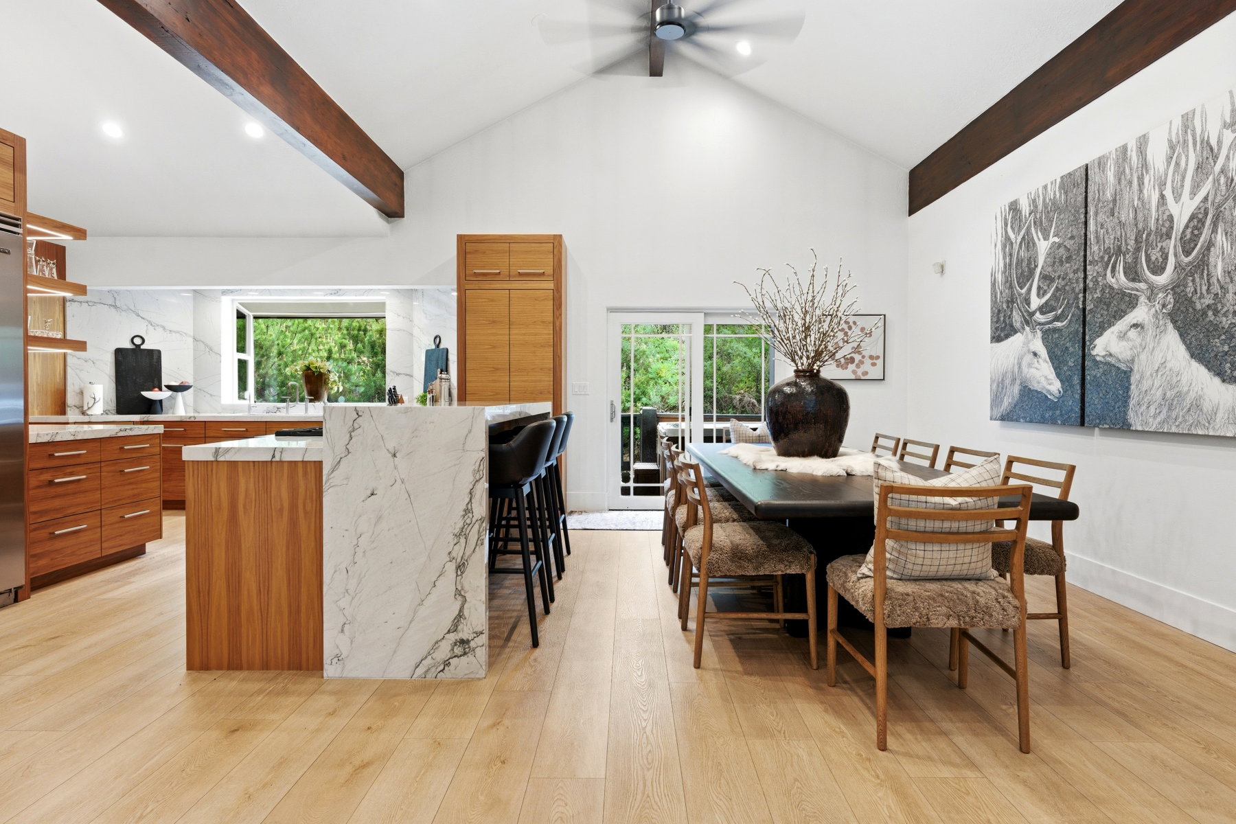 Open-concept kitchen and dining area featuring wood-finish flooring, vaulted ceilings with exposed beams, and a ceiling fan