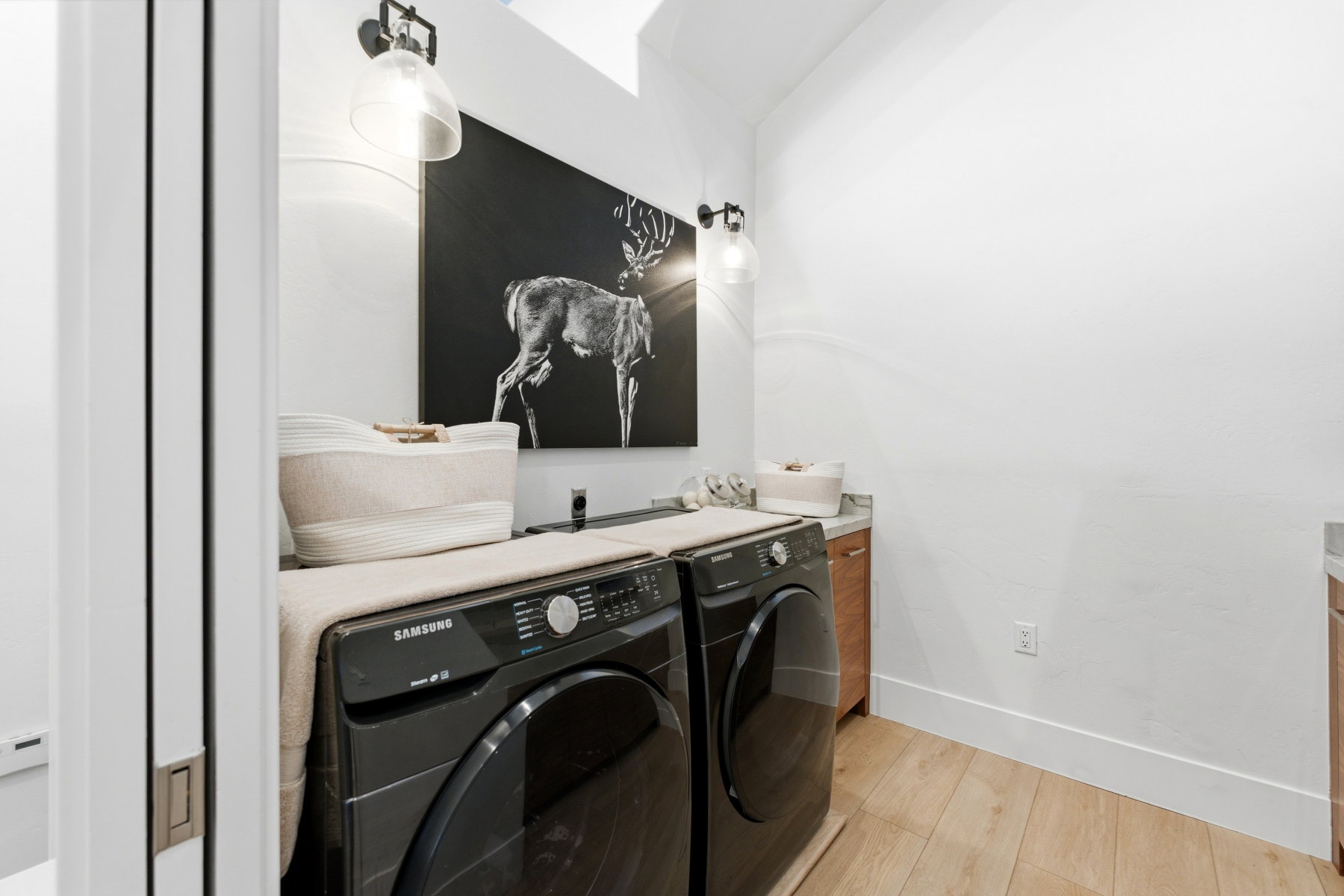 Laundry area featuring wood-finish flooring, white walls, and contemporary wall sconces