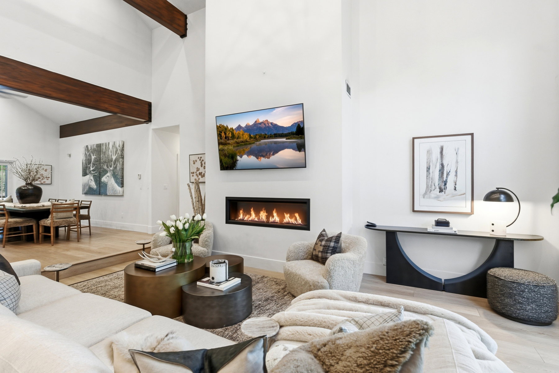 Open-concept living space with a contemporary linear fireplace, high vaulted ceilings with exposed wood beams, and light wood-finish flooring throughout