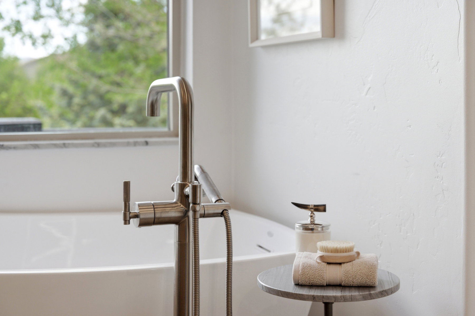 Freestanding bathtub with a floor-mounted brushed nickel faucet and hand spray