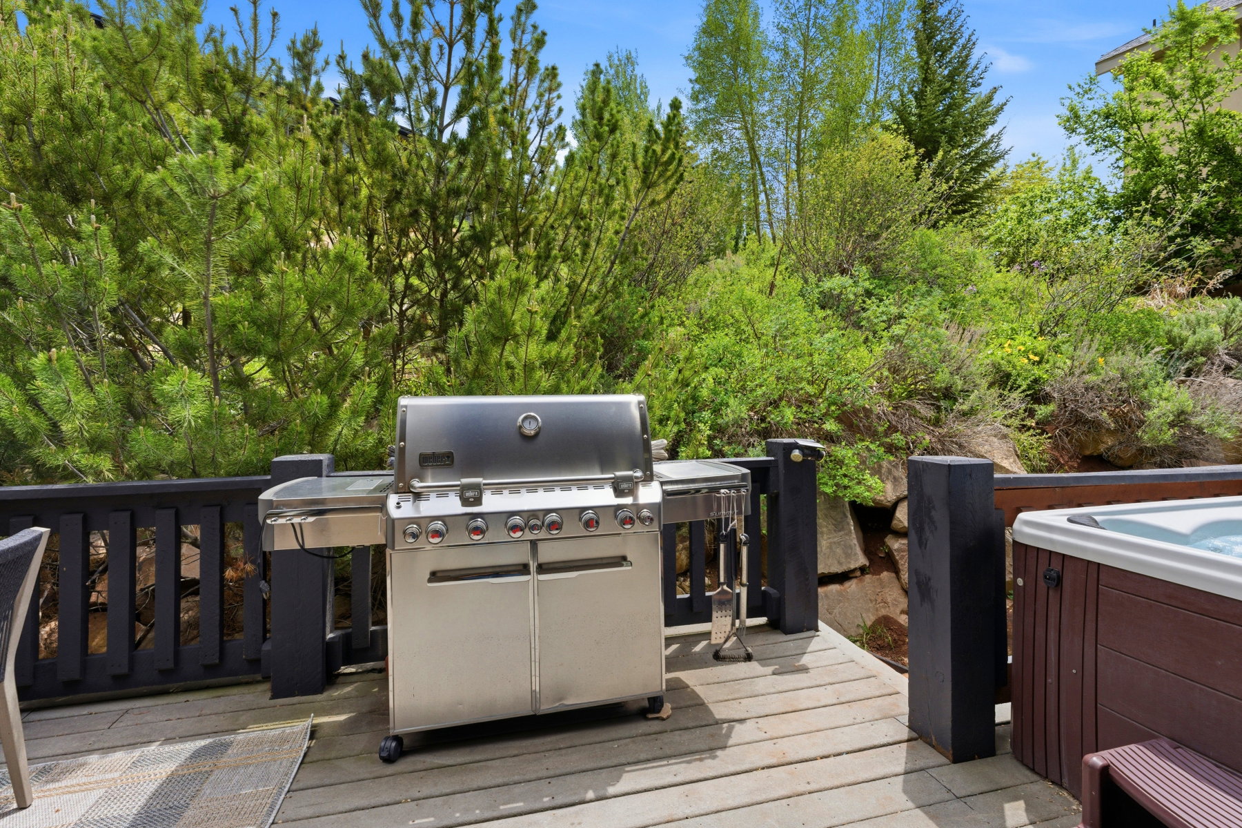 Expansive outdoor deck featuring a stainless steel grill, a built-in hot tub, and a dark-stained wood railing