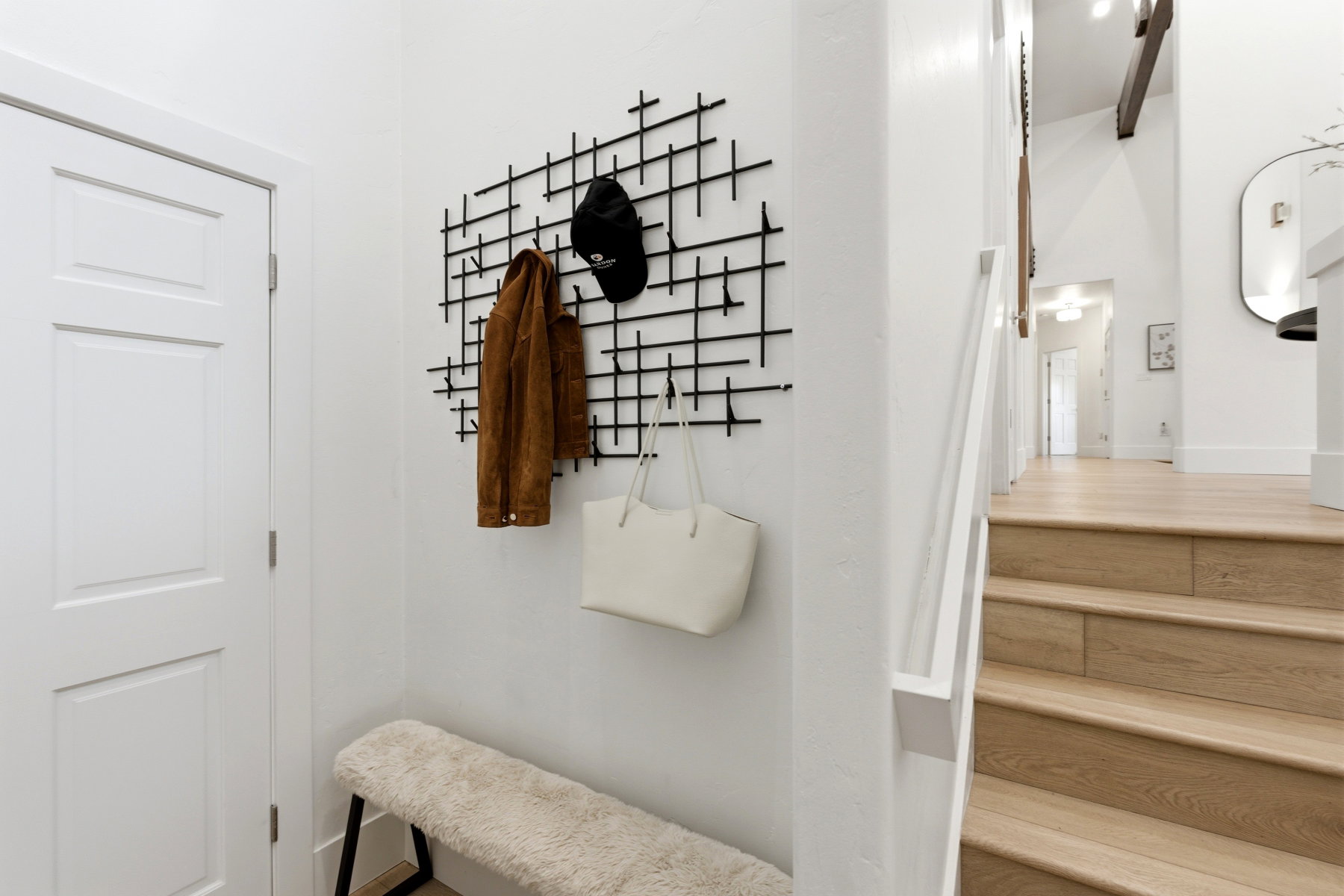 Entryway featuring a white paneled door, light wood-finish flooring, a contemporary black metal wall fixture, and a stairway with a white railing