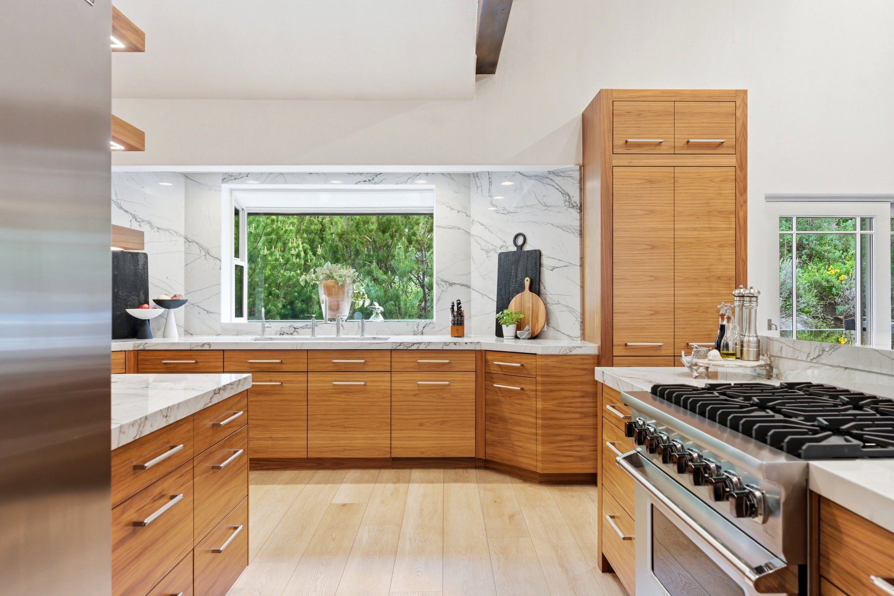 Gourmet kitchen featuring a stainless steel range, white countertops with veining, light wood-finish cabinetry, a large window, and light wood-finish flooring